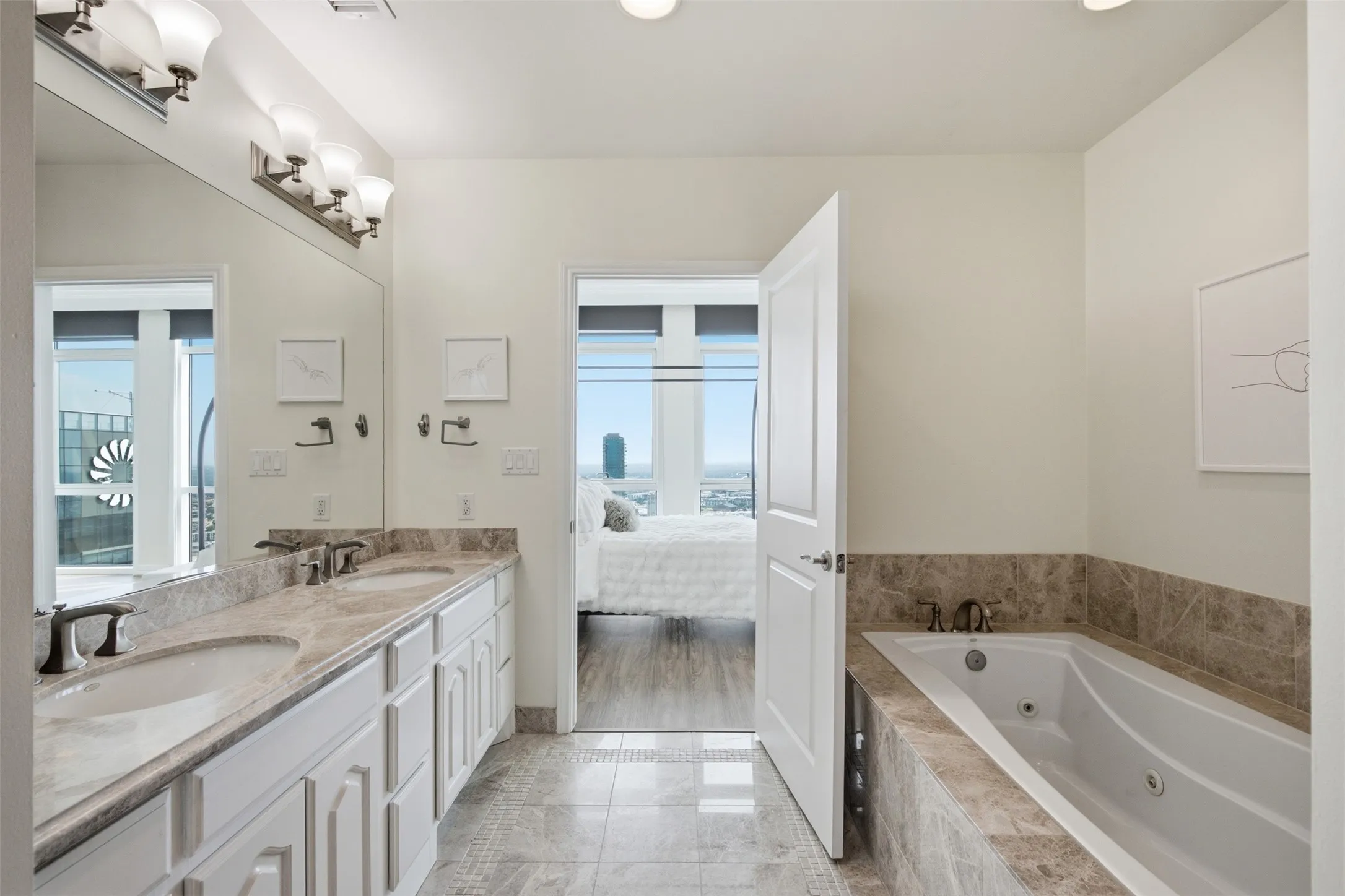 Bathroom featuring a dual vanity with undermount sinks, a large wall-mounted mirror, and an adjacent jetted soaking tub