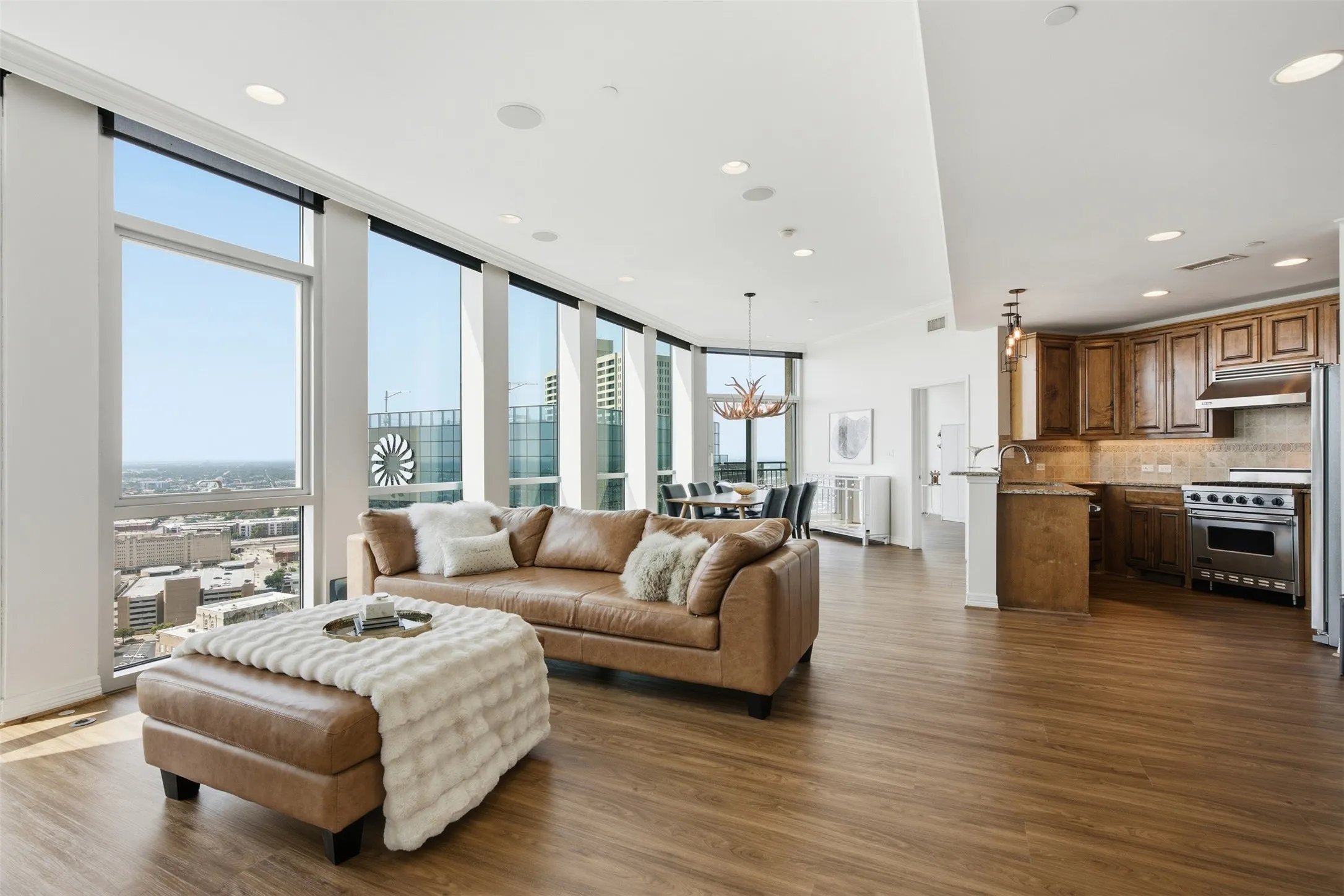 Modern Contemporary living area featuring extensive window walls, wood-finish flooring, recessed lighting, a modern kitchen with wood cabinetry and stainless steel appliances, and an integrated dining space