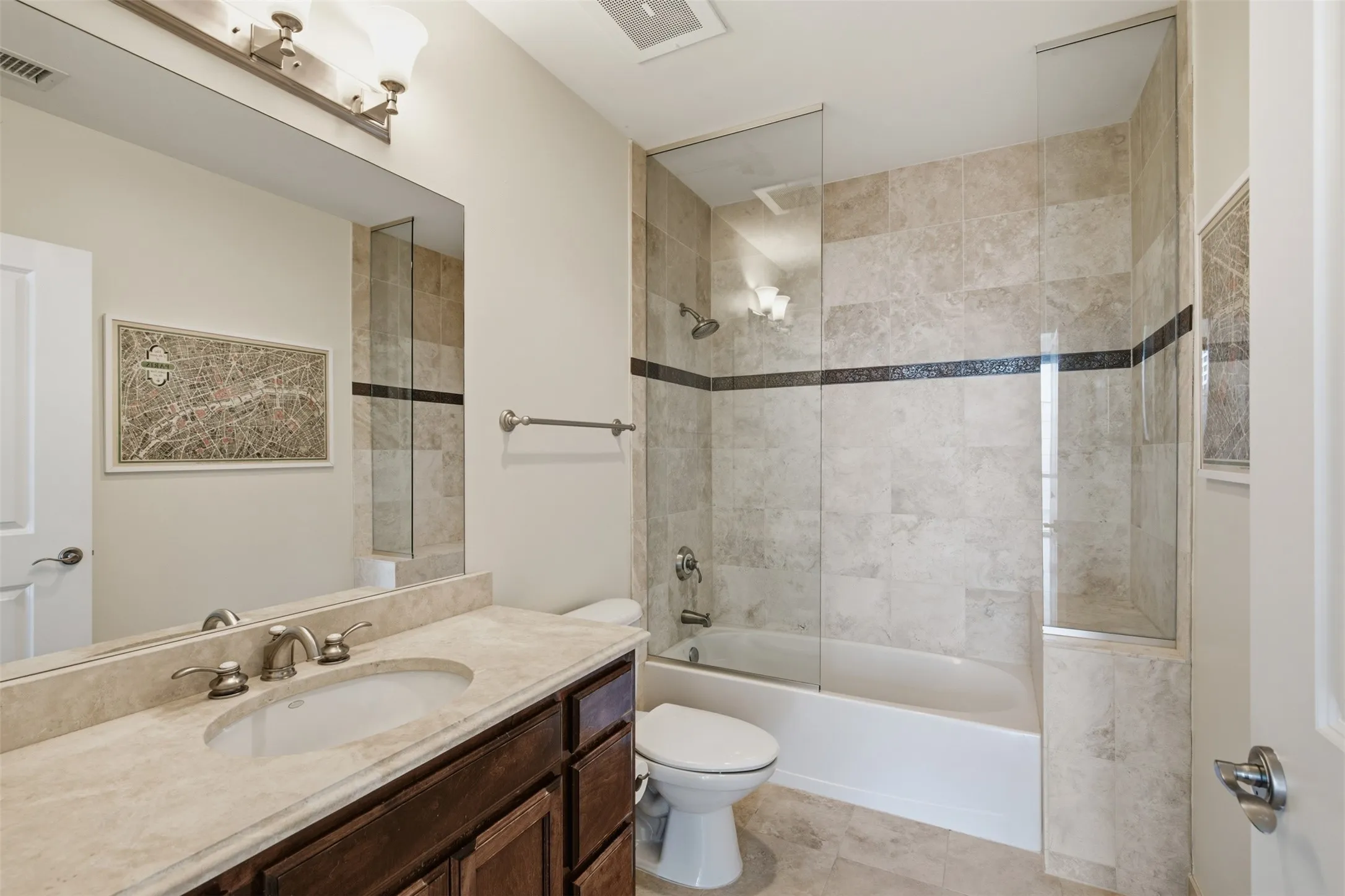 Secondary Bathroom featuring a dark wood-finish vanity, light-toned countertop with an undermount sink, and a combination tub and shower with tile surround and glass enclosure