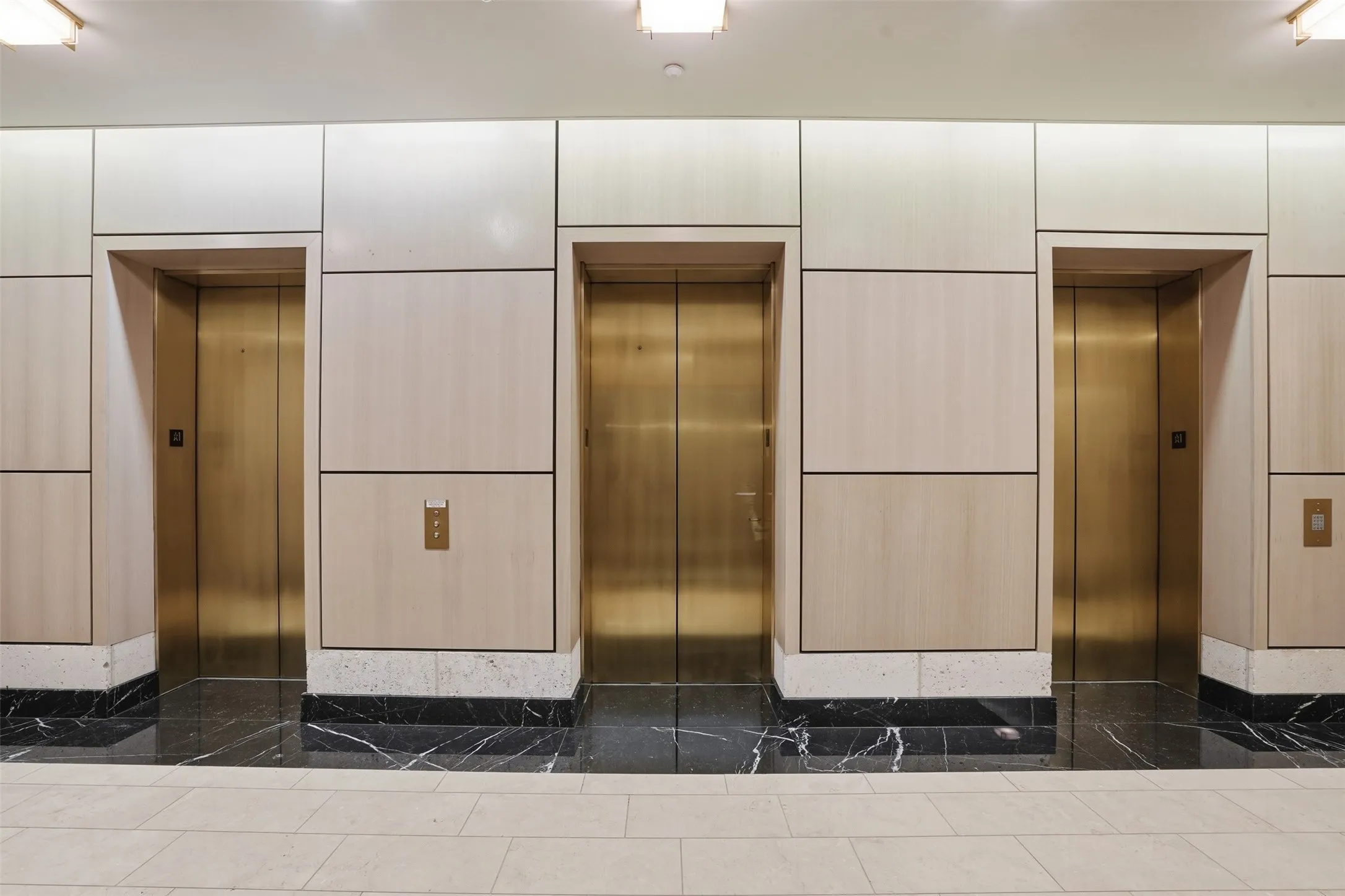 Three elevator doors service floors 20-36 with a brass finish, framed by paneling with a light wood-finish