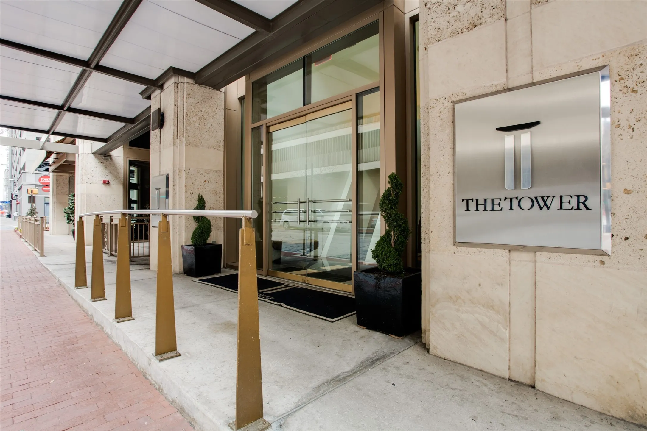 The Tower Building entrance featuring a glass canopy, automatic sliding glass doors, stone facade, and contemporary signage