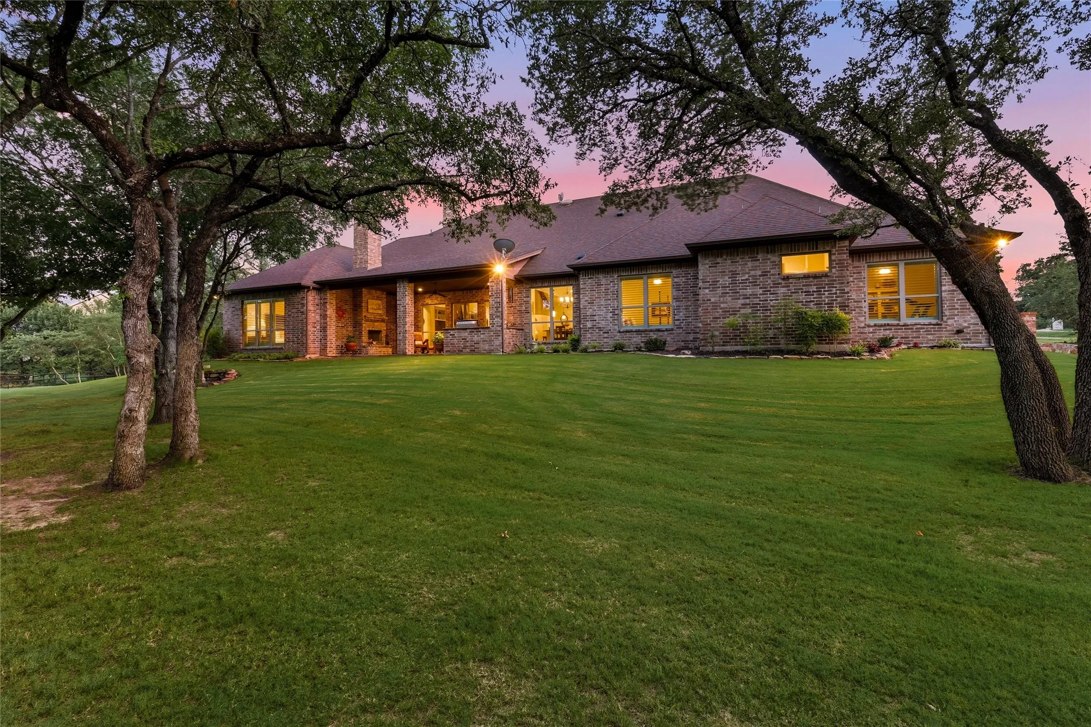 Expansive rear elevation featuring a brick exterior, multiple windows, a covered patio with recessed lighting, and a prominent chimney