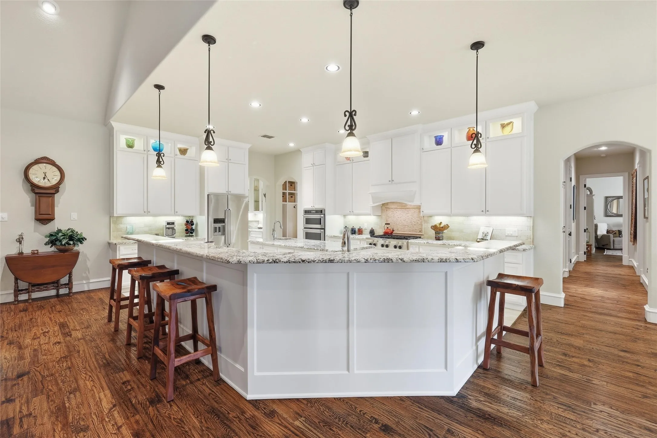 Spacious kitchen featuring an expansive center island with seating, white cabinetry, integrated stainless steel appliances, recessed lighting, and wood-finish flooring