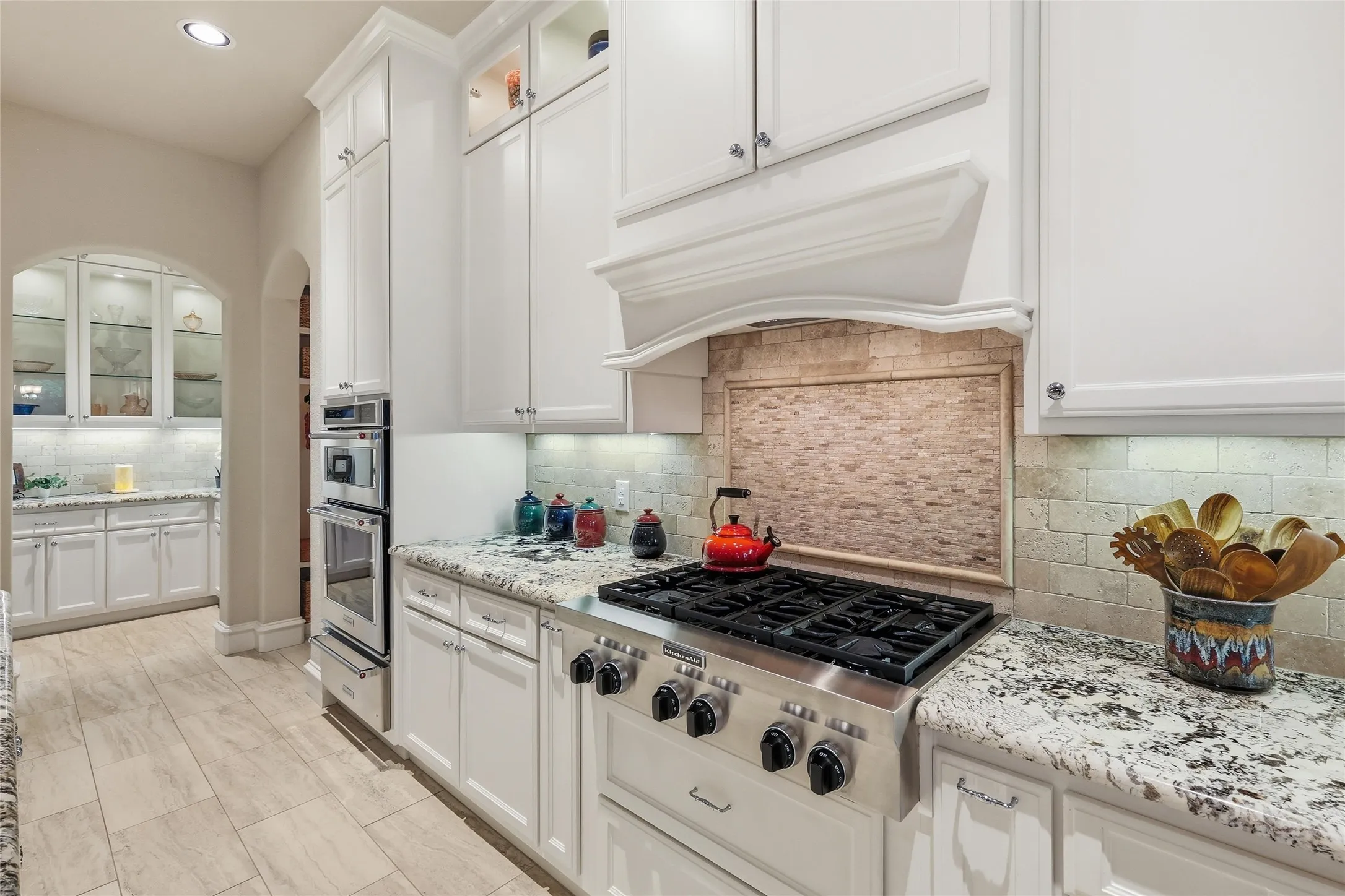 Bright kitchen featuring white cabinetry, stone countertops, a stainless steel gas range, double wall ovens, and a tile backsplash