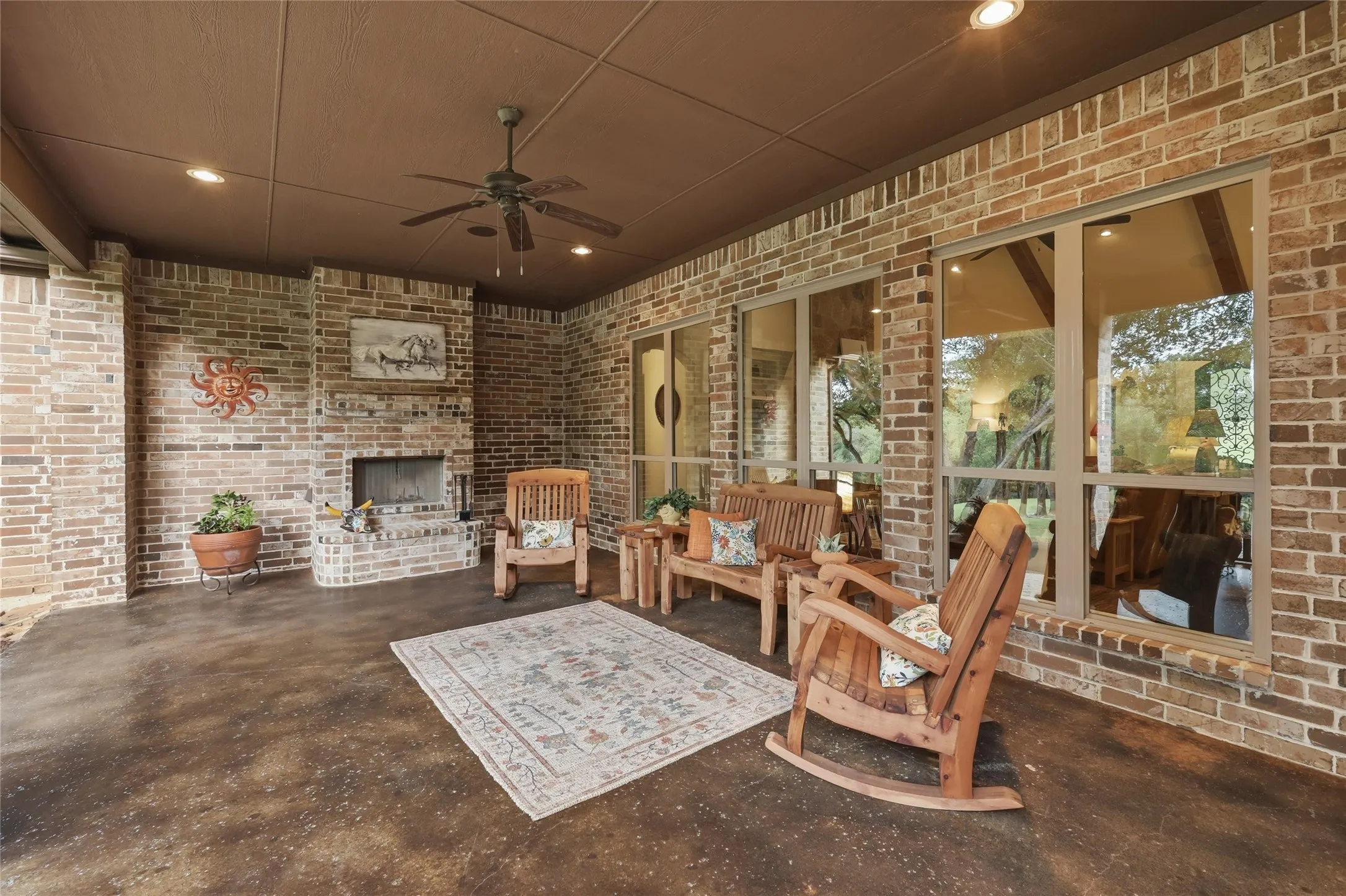 Covered patio featuring a brick fireplace with hearth, recessed lighting, ceiling fan, and large windows