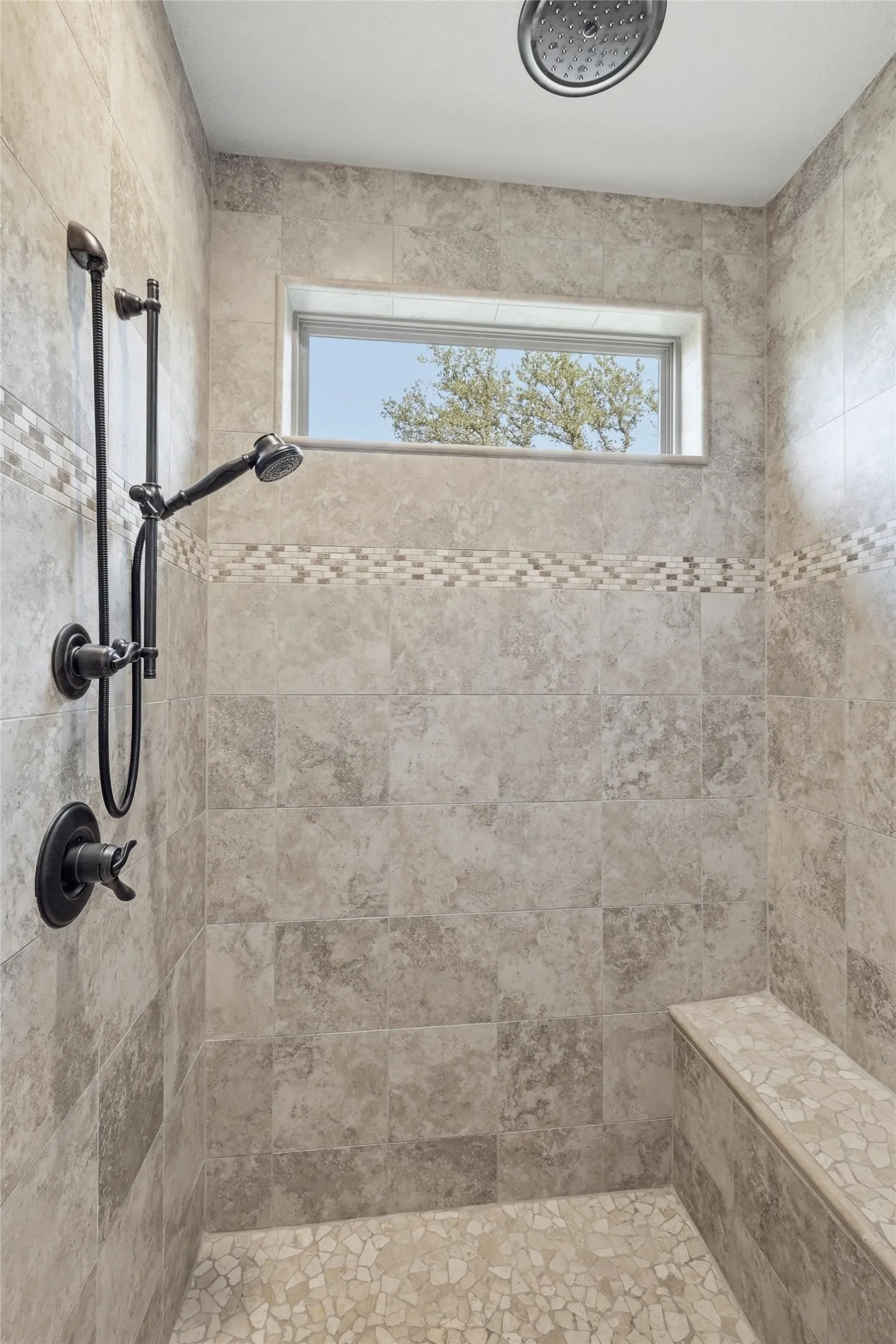 Tiled shower stall featuring a rainfall showerhead, handheld shower fixture, and an integrated bench