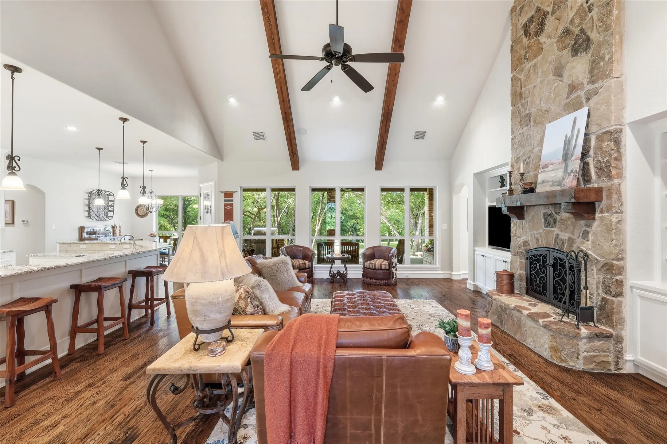 Spacious living area featuring a stone fireplace with a substantial wood mantel, vaulted ceilings with exposed wood beams, and rich wood-finish flooring