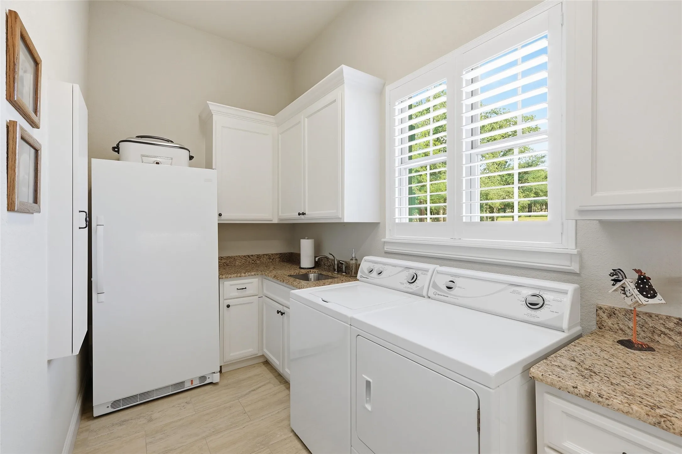 Laundry room featuring light-toned flooring, white cabinetry, granite countertops, and a window with plantation shutters, don't miss the sink !