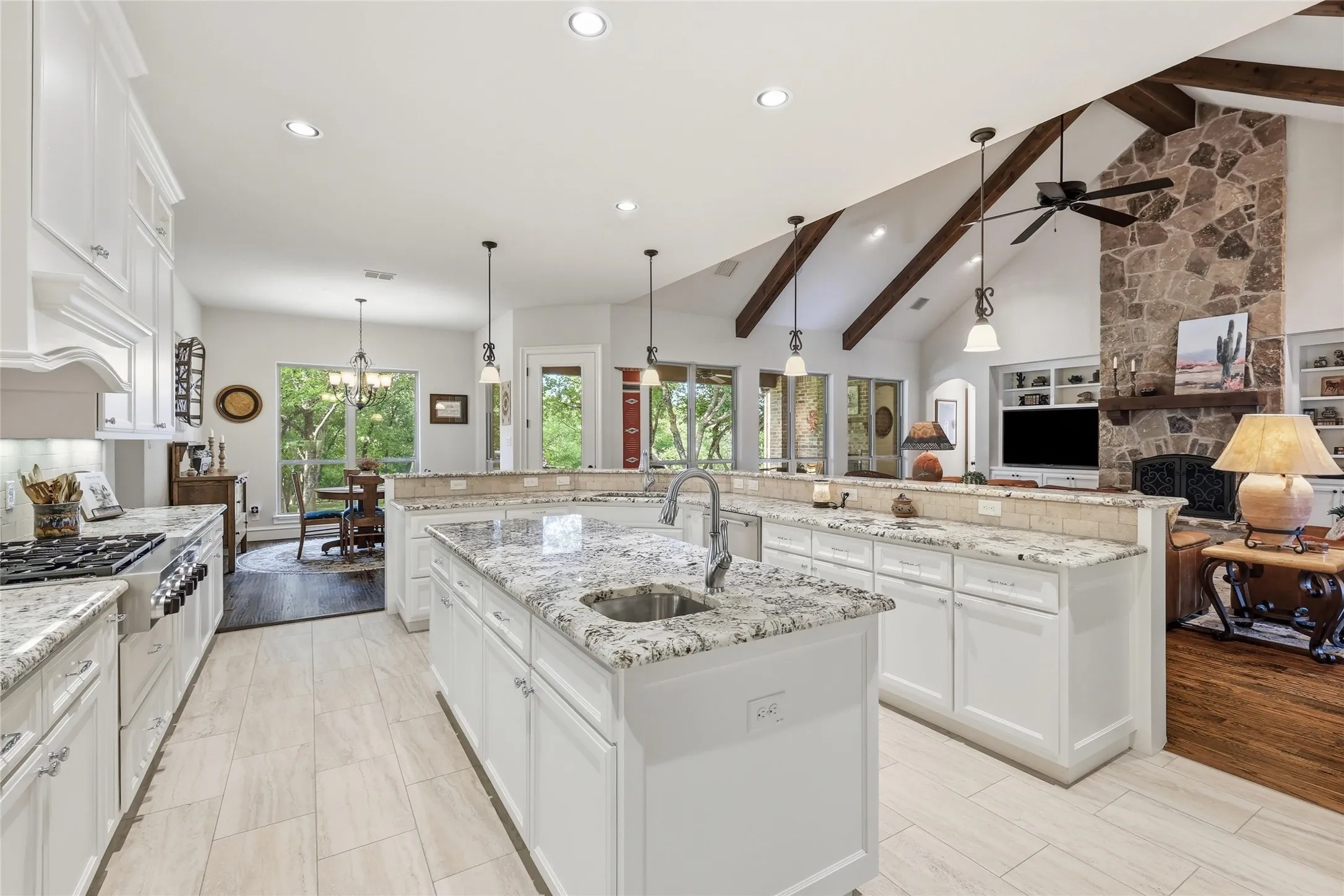 Open-concept kitchen featuring an oversized island with an undermount sink, granite countertops, white cabinetry, and wood-finish tile flooring
