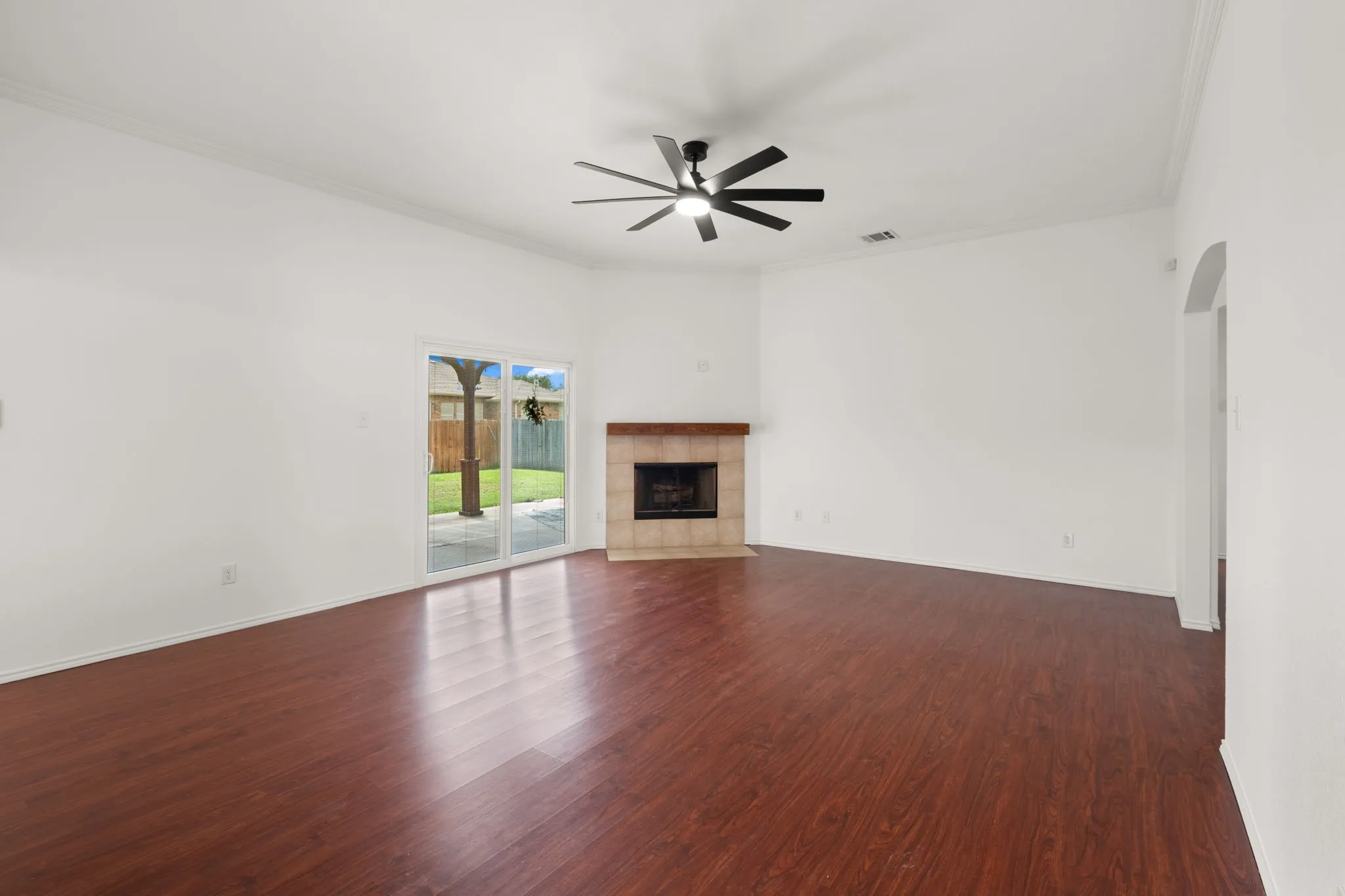 Spacious interior with wood-finish flooring, a contemporary ceiling fan, and a tiled fireplace with a wood mantle