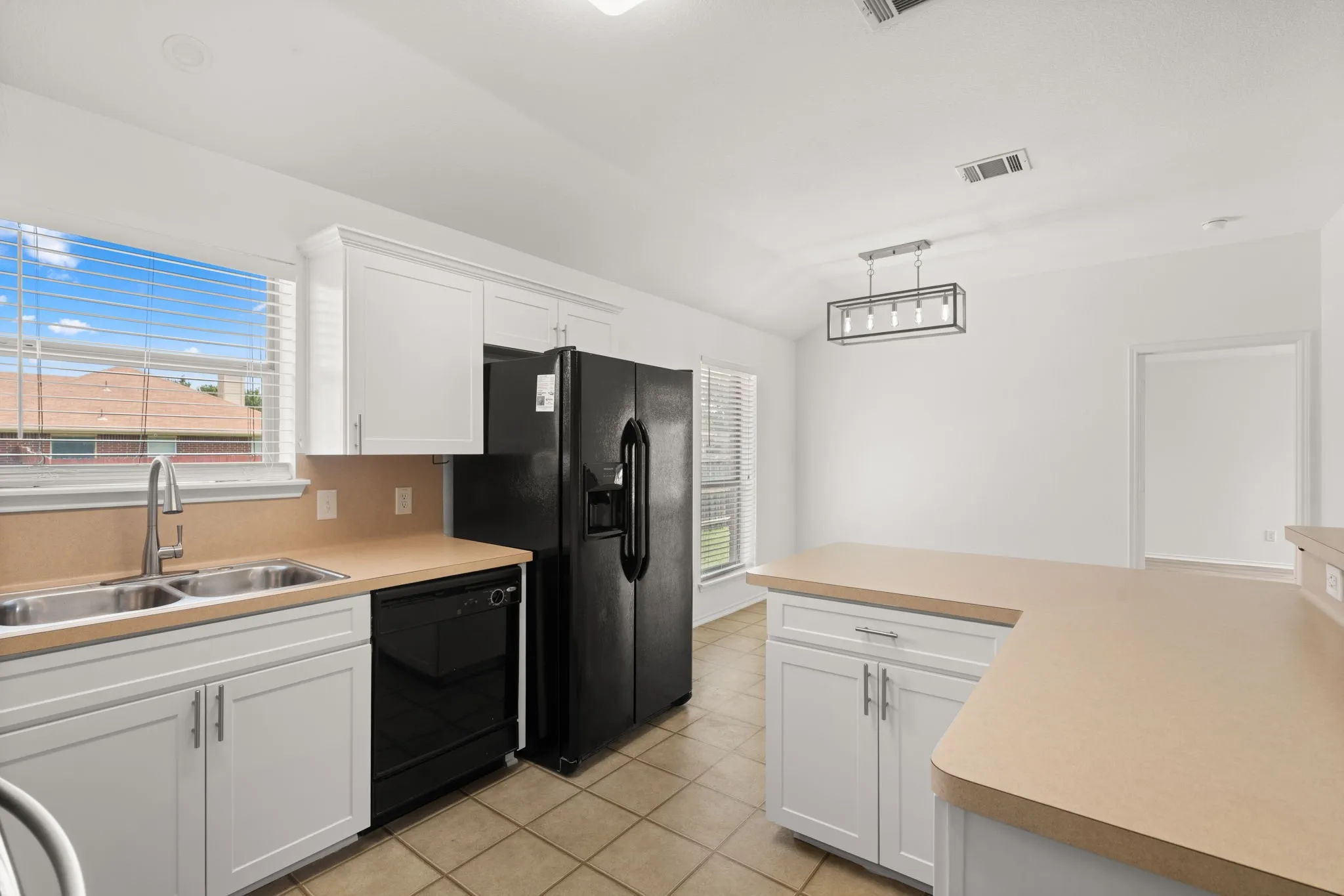 Kitchen featuring white shaker cabinetry, an integrated double basin sink, black appliances, and neutral countertops