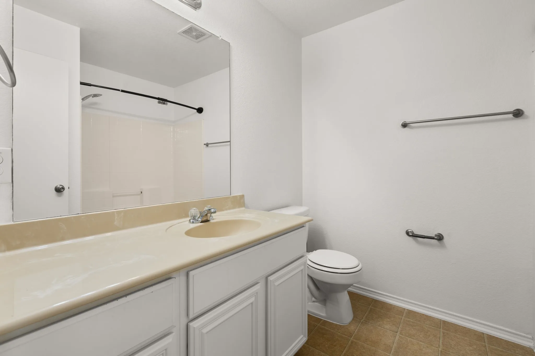 Bathroom featuring a vanity with a light-toned countertop and integrated sink, white cabinetry, a large wall-mounted mirror, a commode, and tiled flooring