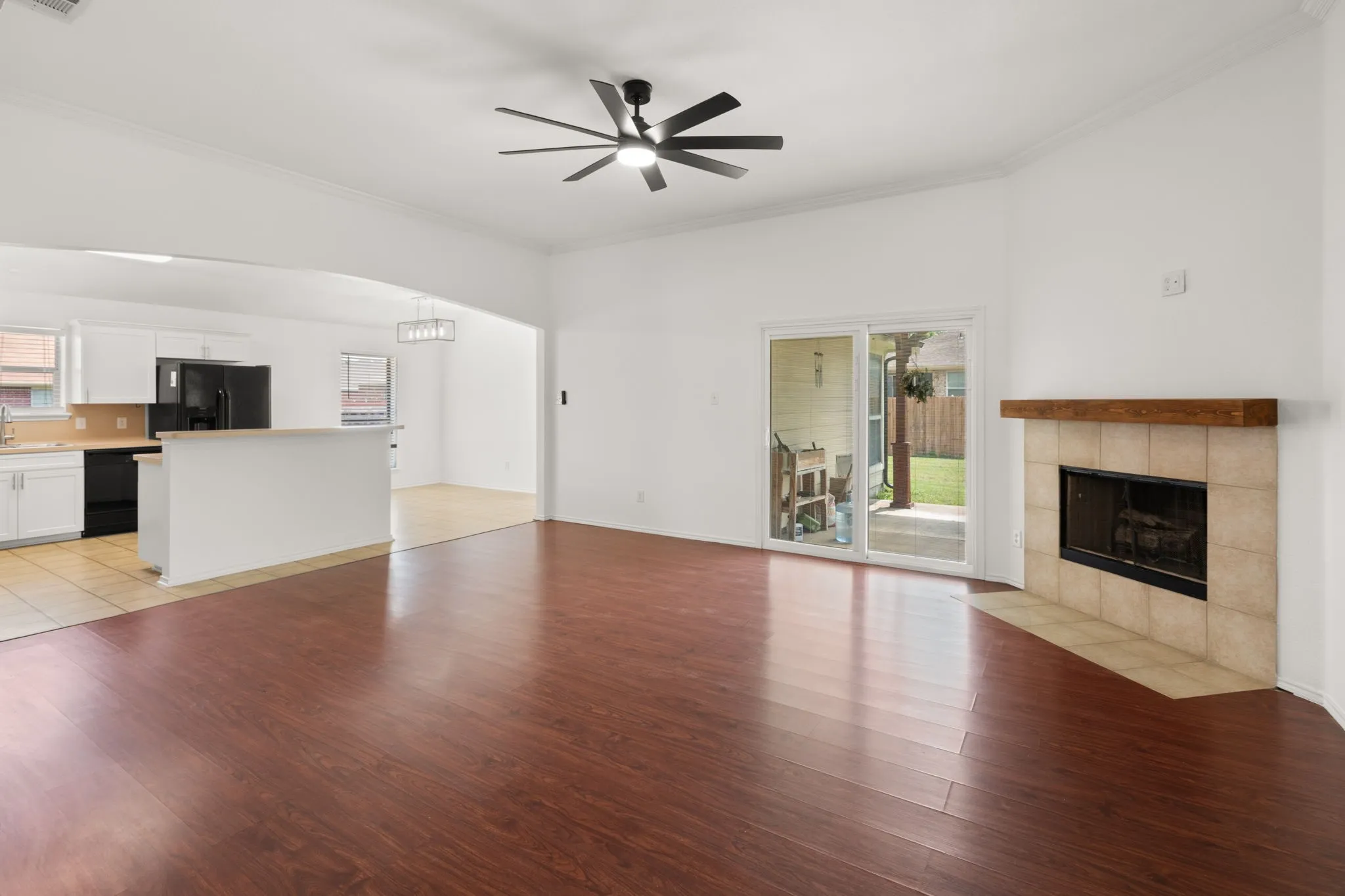 Spacious living area featuring wood-finish flooring, a ceiling fan, and a fireplace with a tile surround and wood mantel