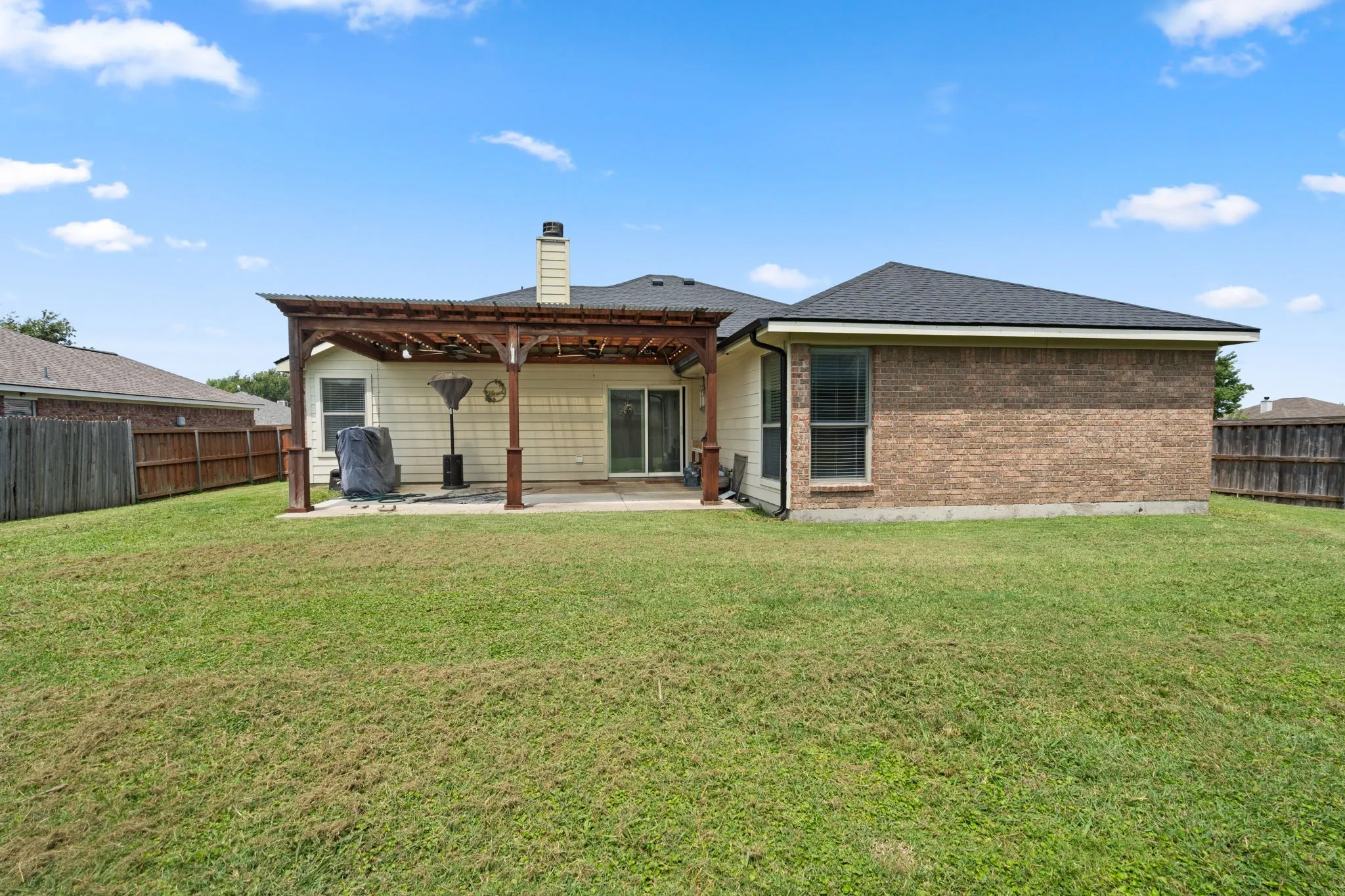 Rear exterior featuring a covered patio with a pergola, brick and siding facade, and a private wooden fence