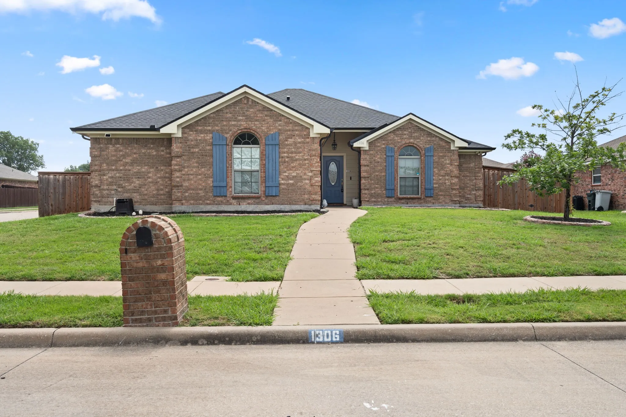Brick facade home featuring a dark shingle roof, blue decorative shutters, and a matching blue entry door