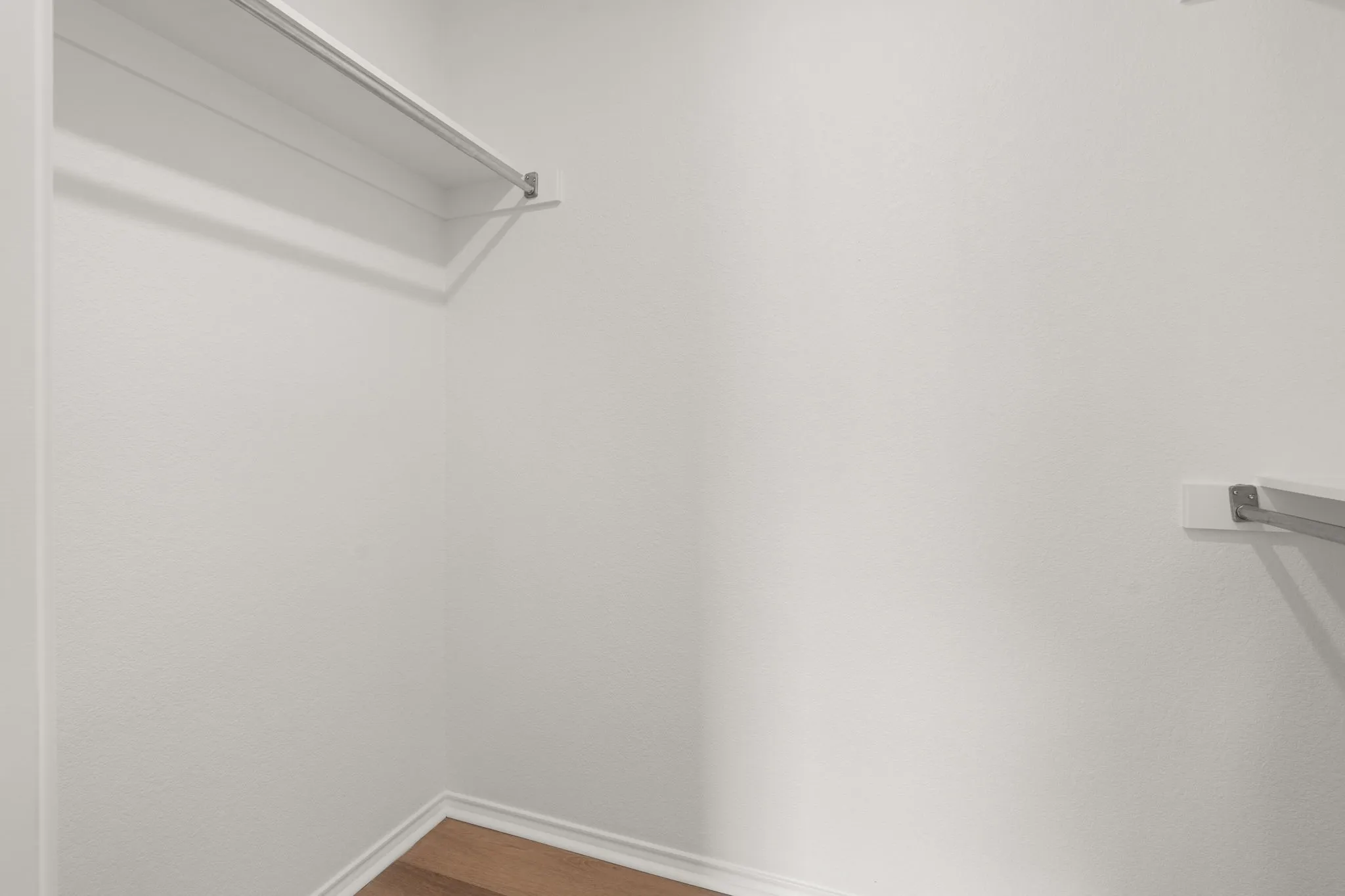 Walk-in closet featuring white painted walls, wood-finish flooring, and two chrome clothing rods