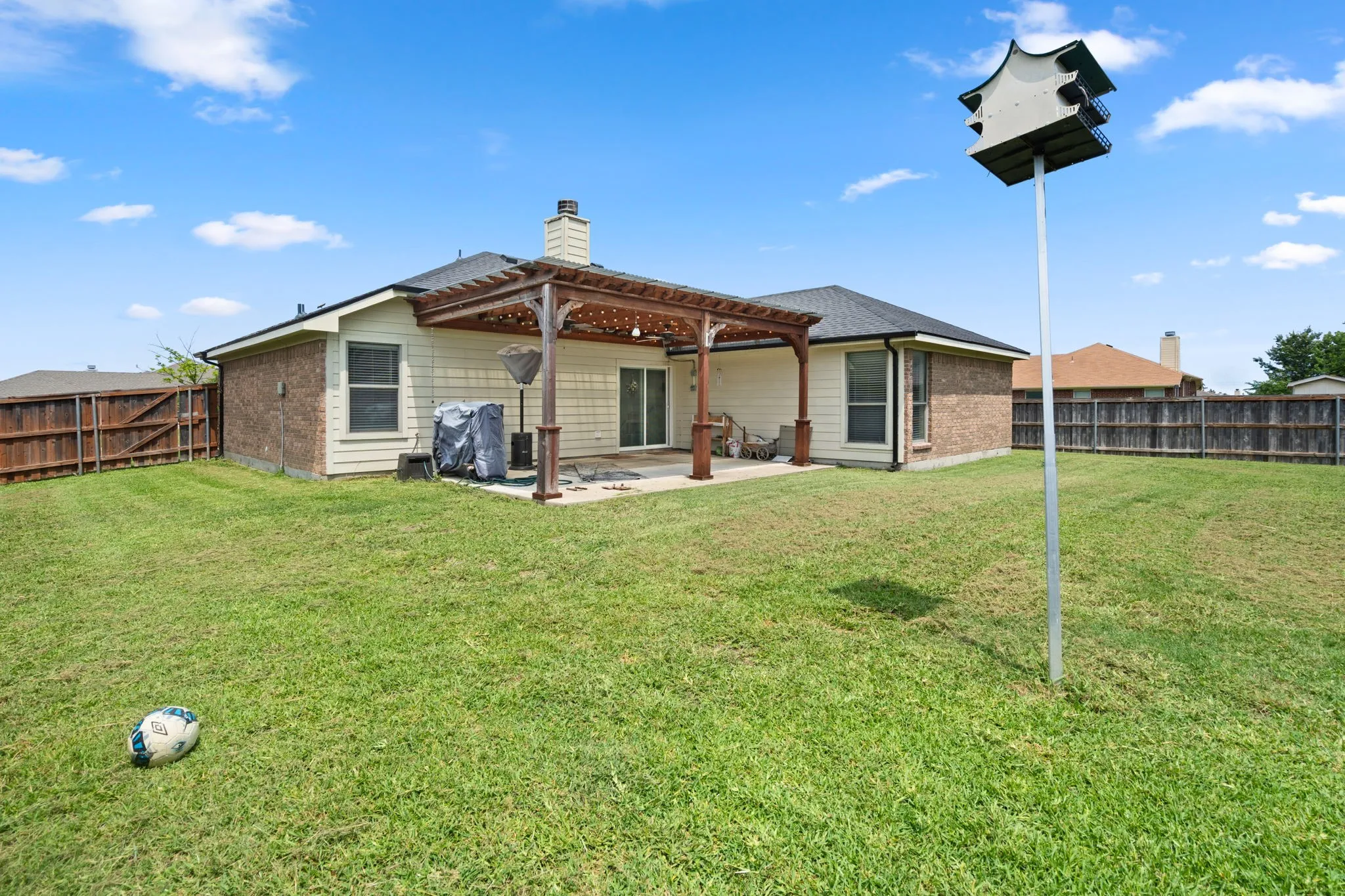 Expansive rear yard featuring a wood pergola over a concrete patio, a brick and siding exterior, and a wood privacy fence