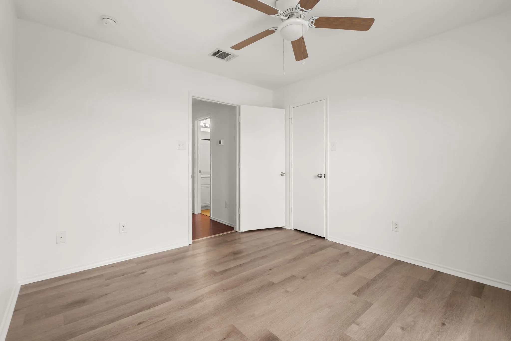 Room featuring light wood-finish flooring, white walls, and a ceiling fan with wood-tone blades