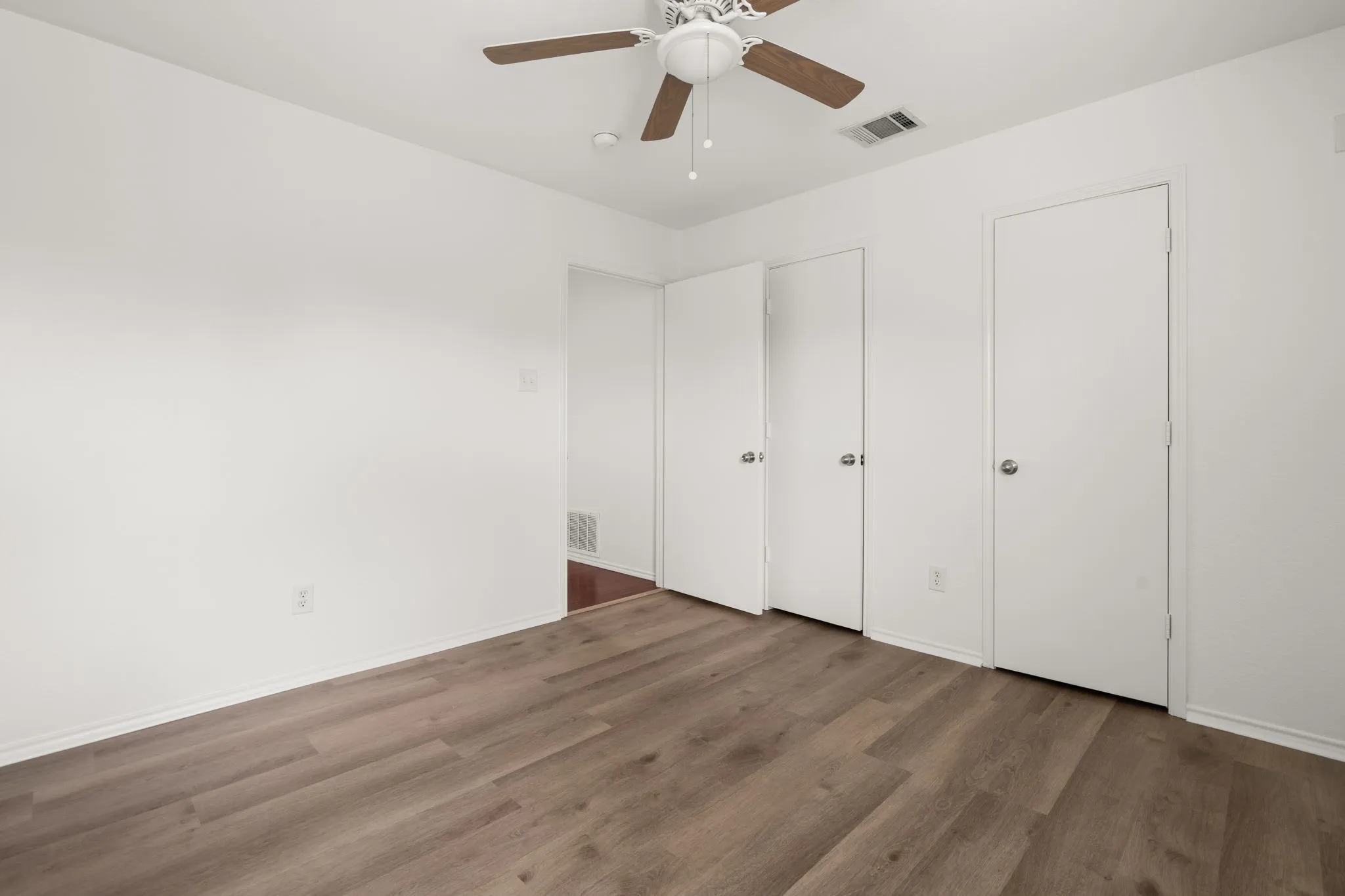 Interior room featuring wood-finish flooring, crisp white walls, and a ceiling fan with light fixture