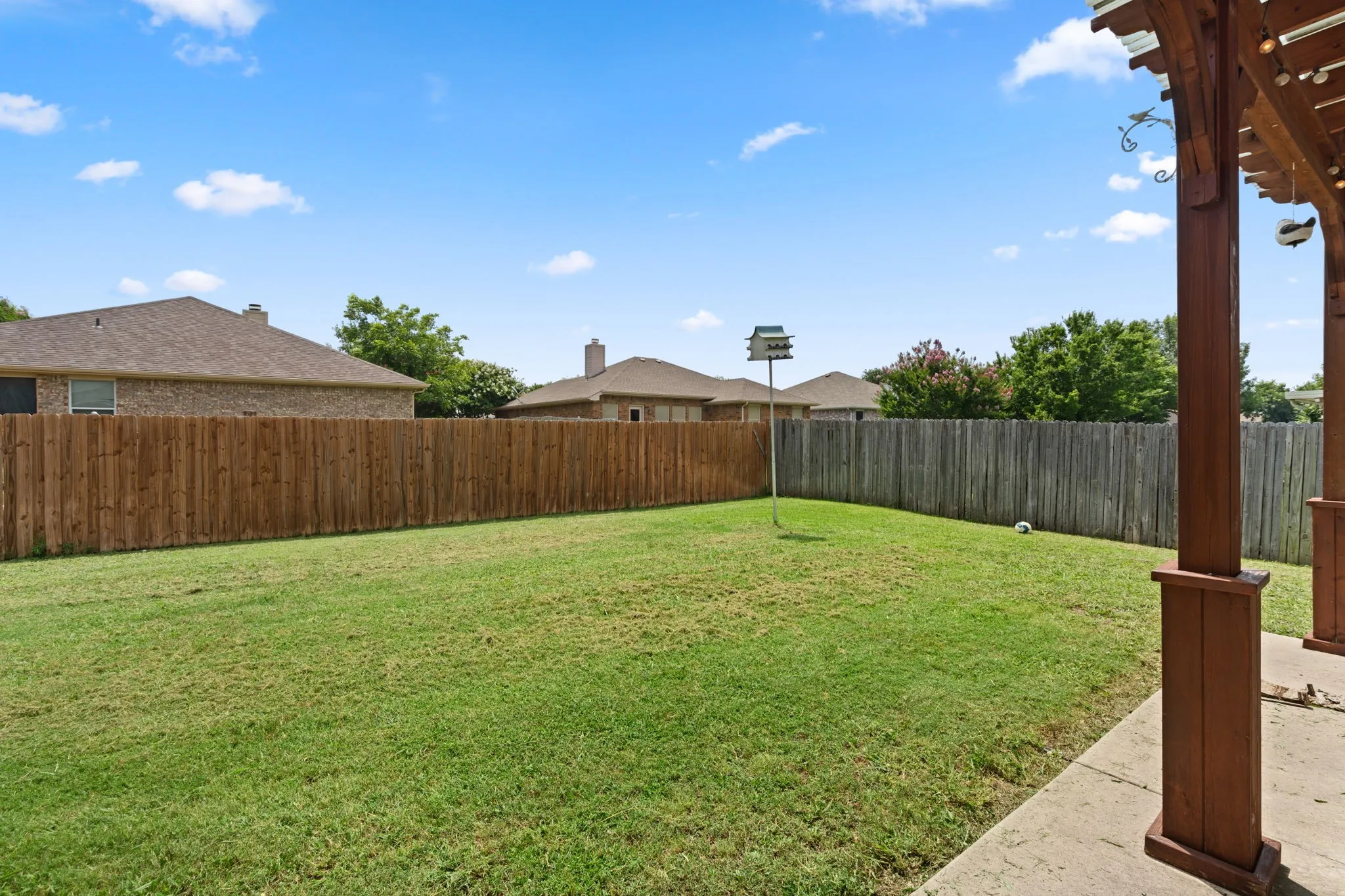 Expansive backyard featuring a manicured lawn, a wooden privacy fence, and a concrete patio with a dark wood pergola