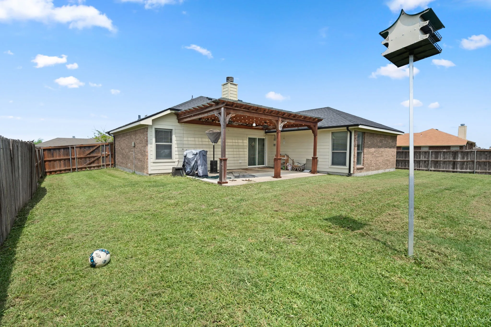 Expansive fenced backyard featuring a wood pergola-covered patio, sliding glass door access, and a brick and siding exterior
