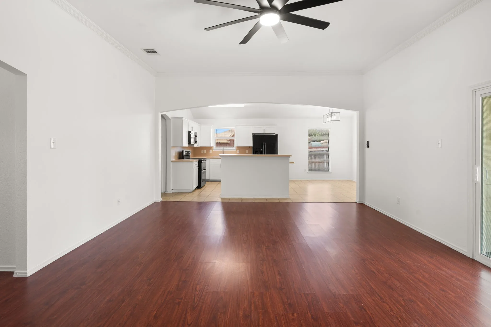 Spacious living area featuring wood-finish flooring, white walls, and a ceiling fan with integrated lighting