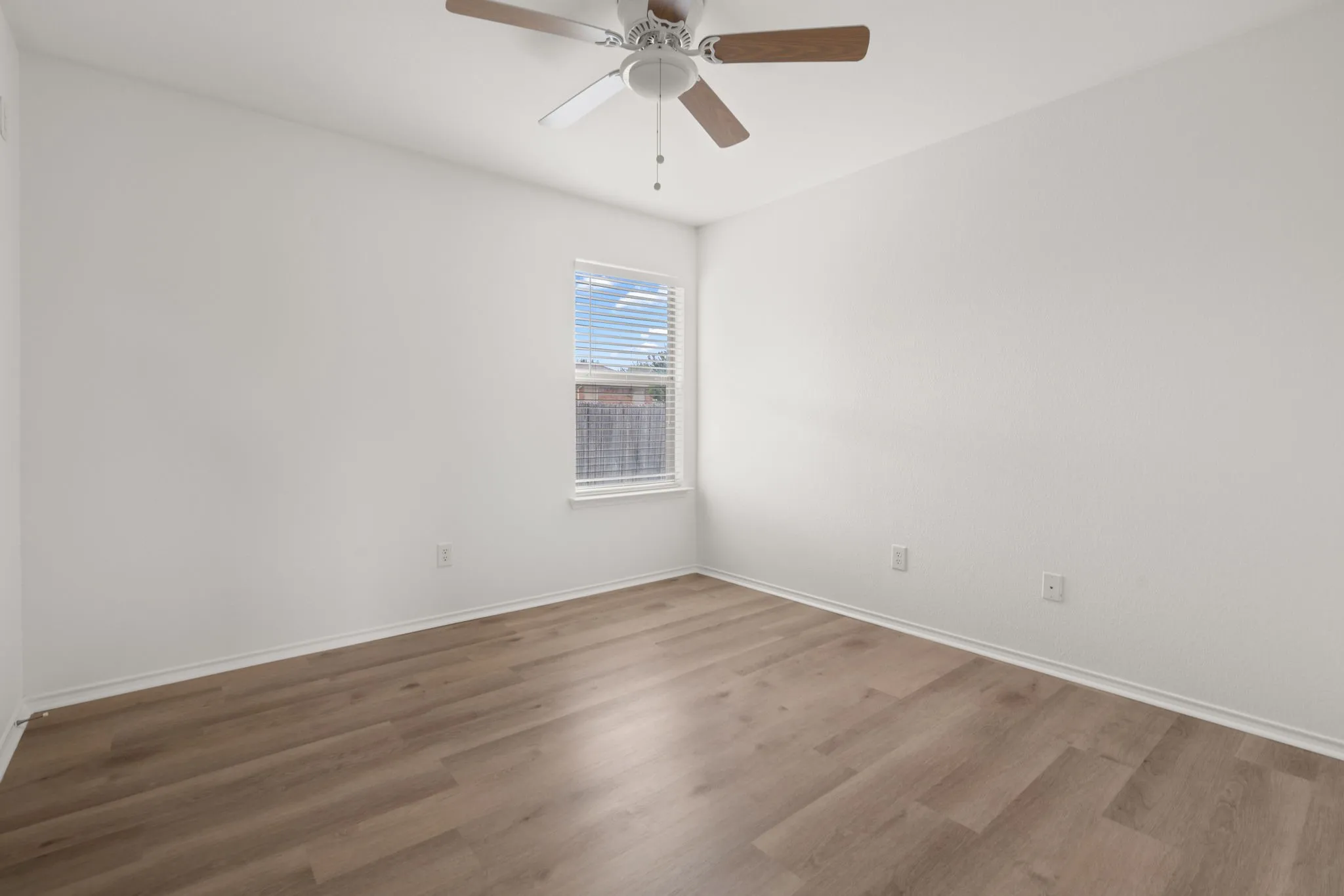 Interior space featuring wood-finish flooring, white baseboards, and a ceiling fan with wood-look blades