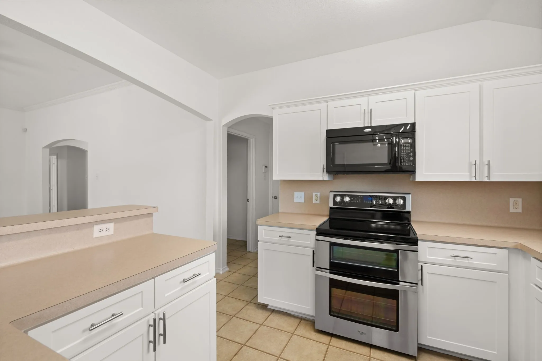 Well-appointed kitchen featuring white cabinetry, light-toned countertops, and a full suite of stainless steel and black appliances