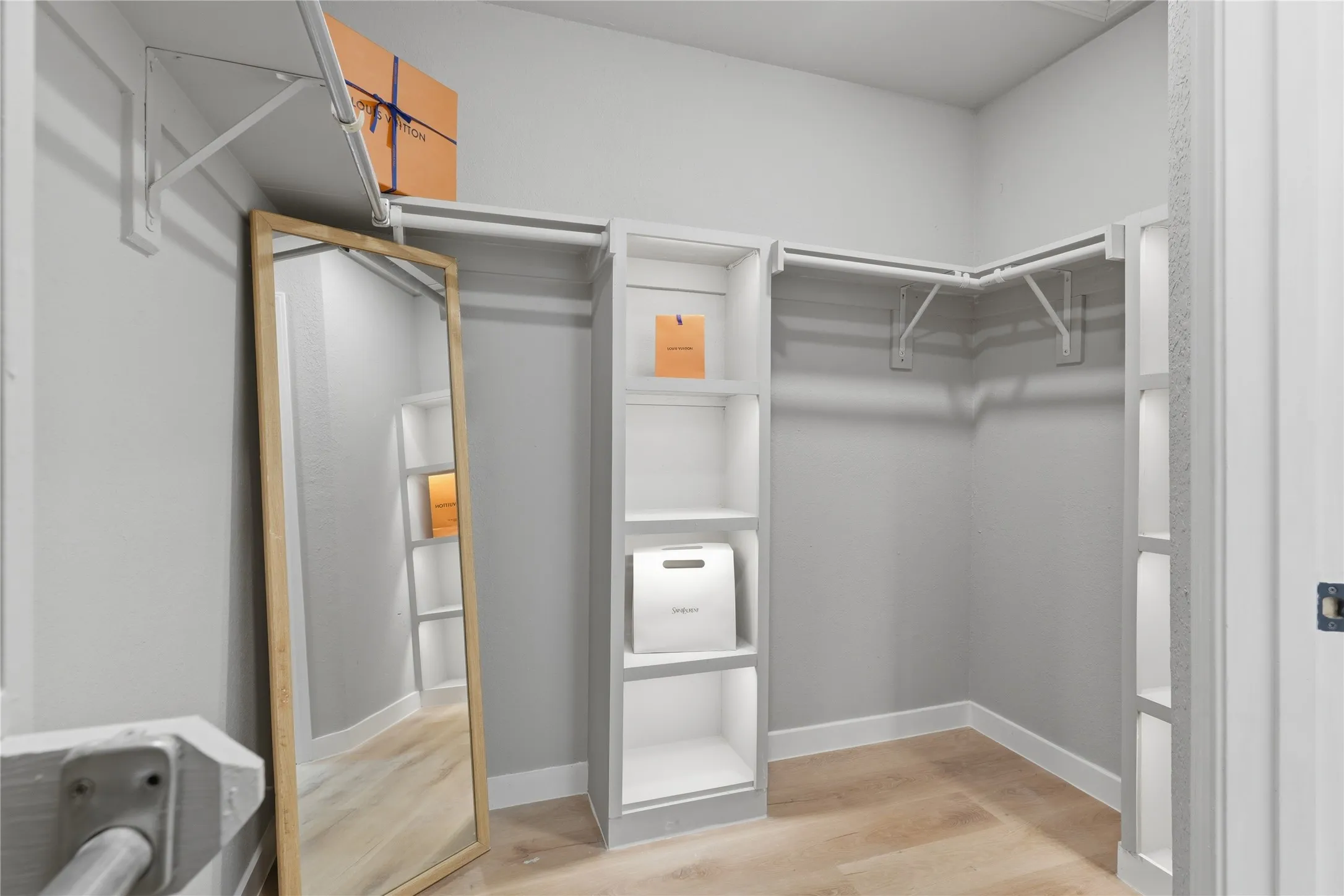 Walk-in closet featuring light wood-finish flooring, white walls, and a multi-level storage system with shelving and hanging rods