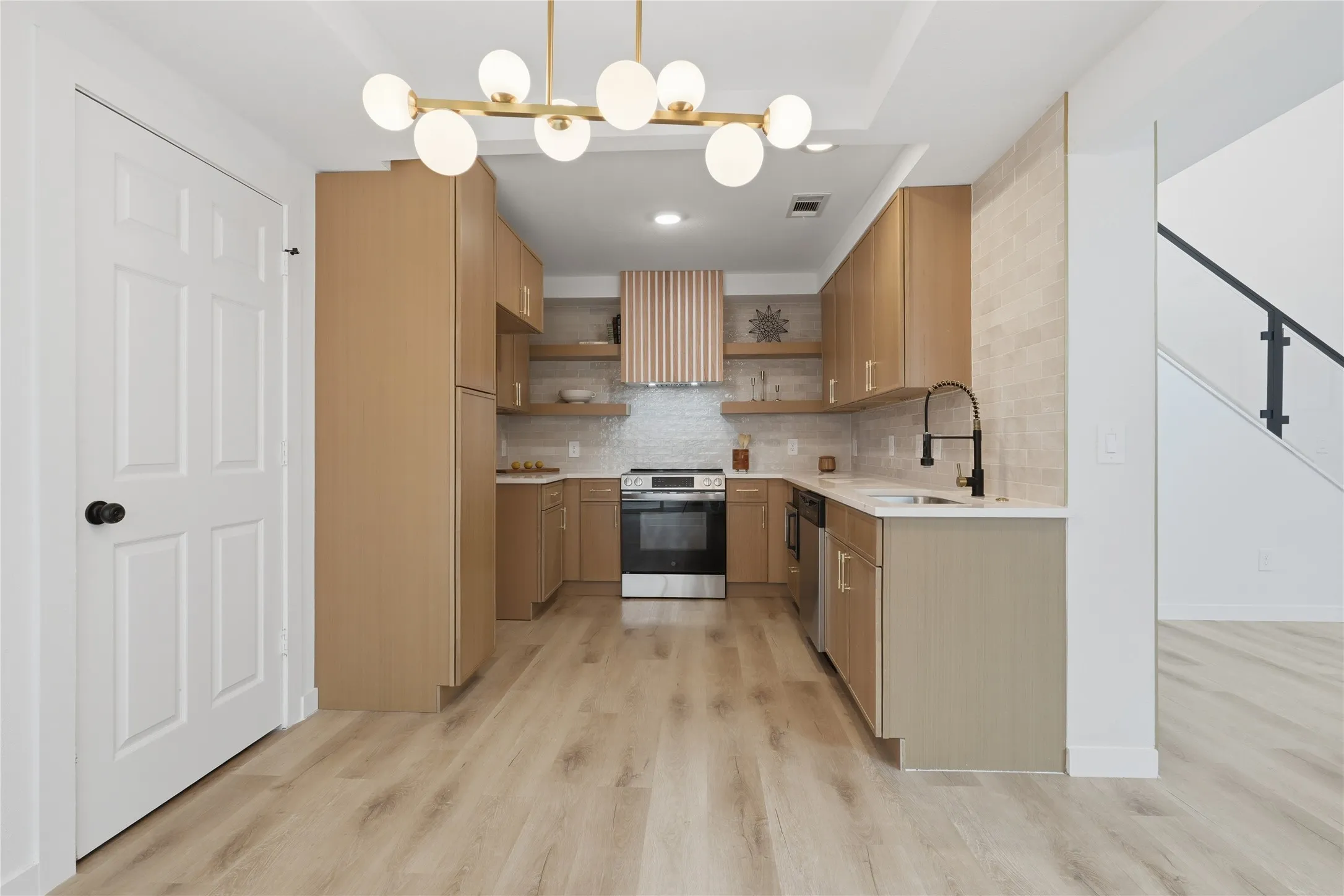 Modern kitchen featuring light wood-finish cabinetry, stainless steel appliances, a matte black faucet, and a contemporary chandelier