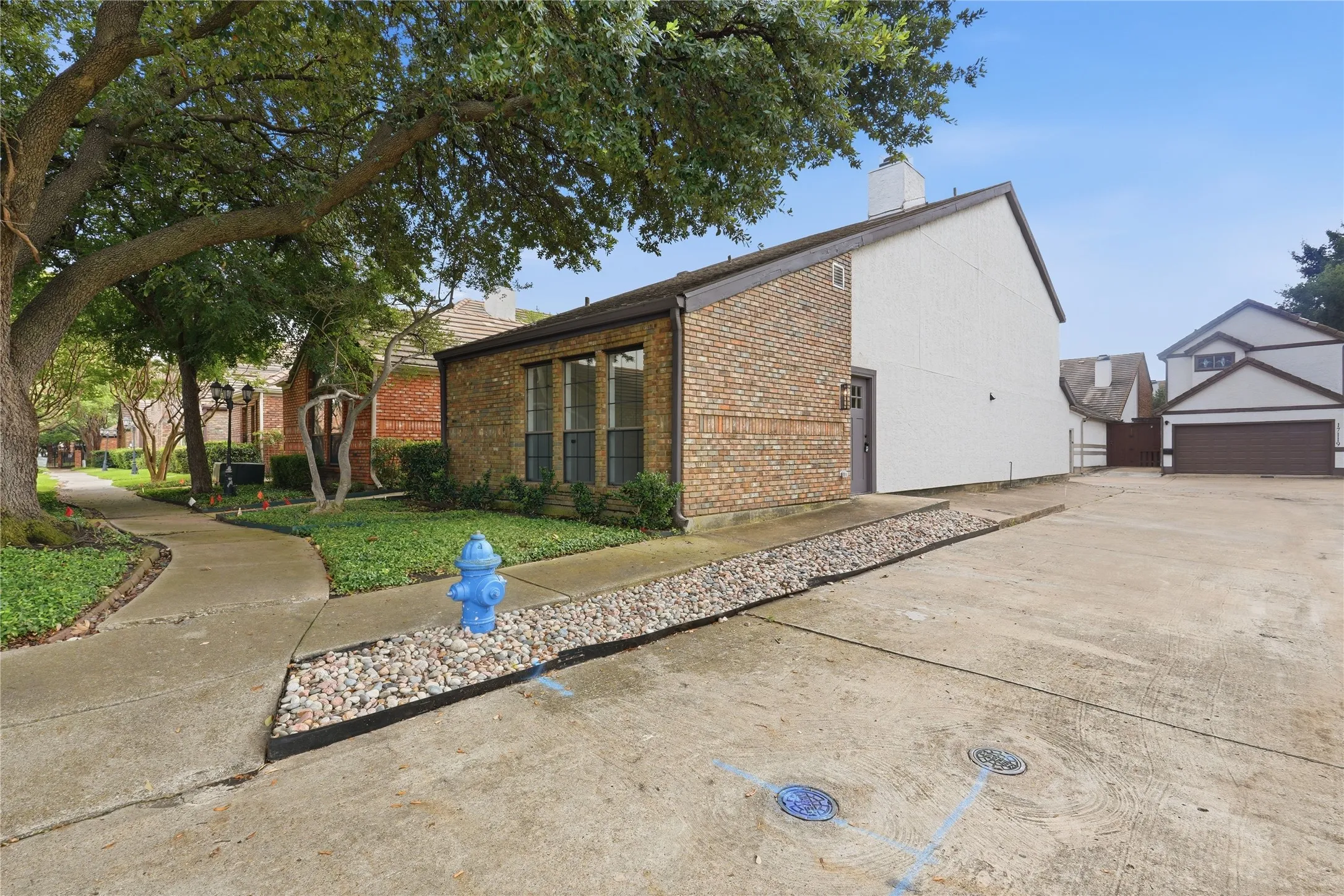 Brick and siding exterior featuring large windows, a paved driveway, and established trees