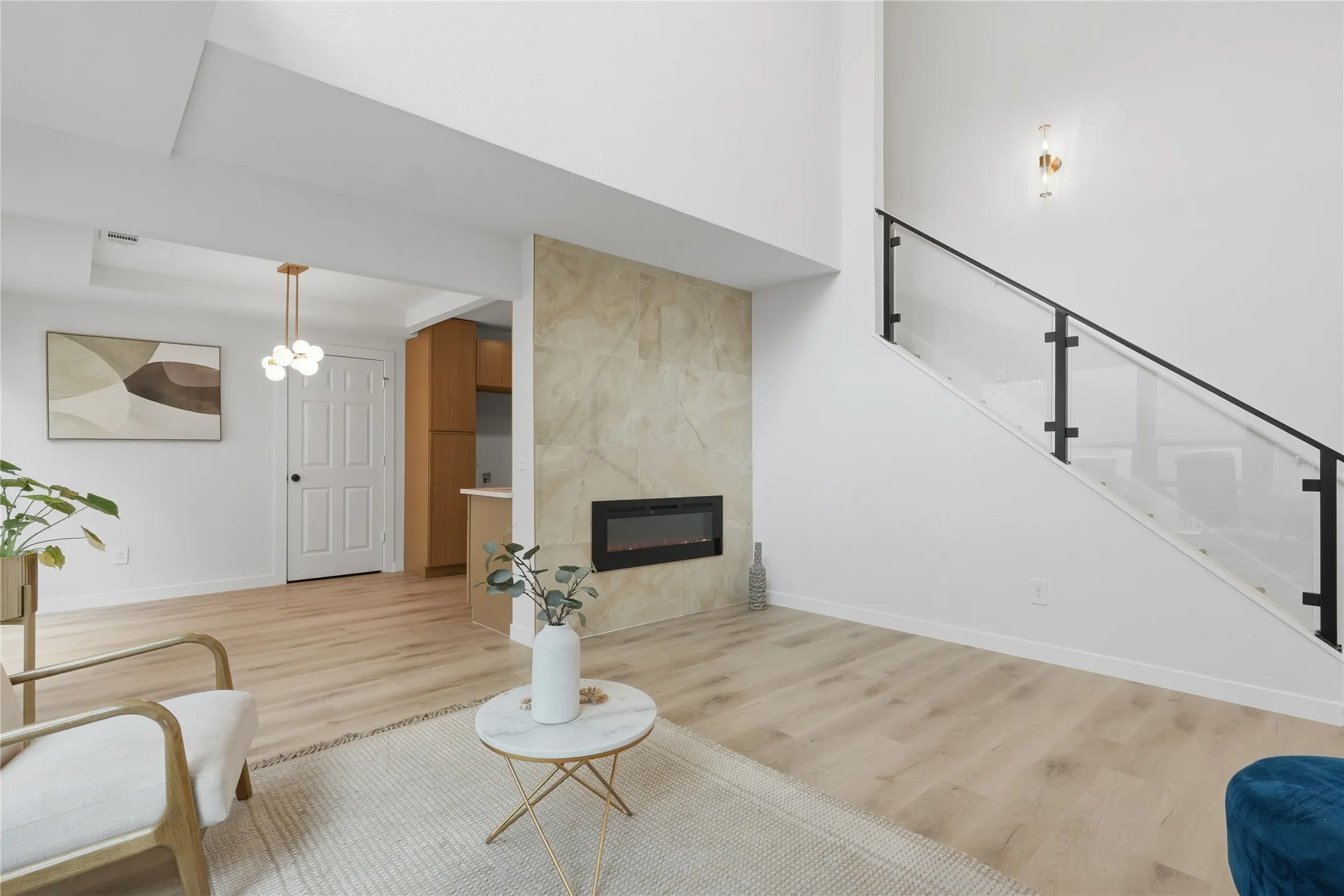 Living area featuring a floor-to-ceiling fireplace with stone-finish surround, light wood-finish flooring, and a modern glass and black metal staircase railing
