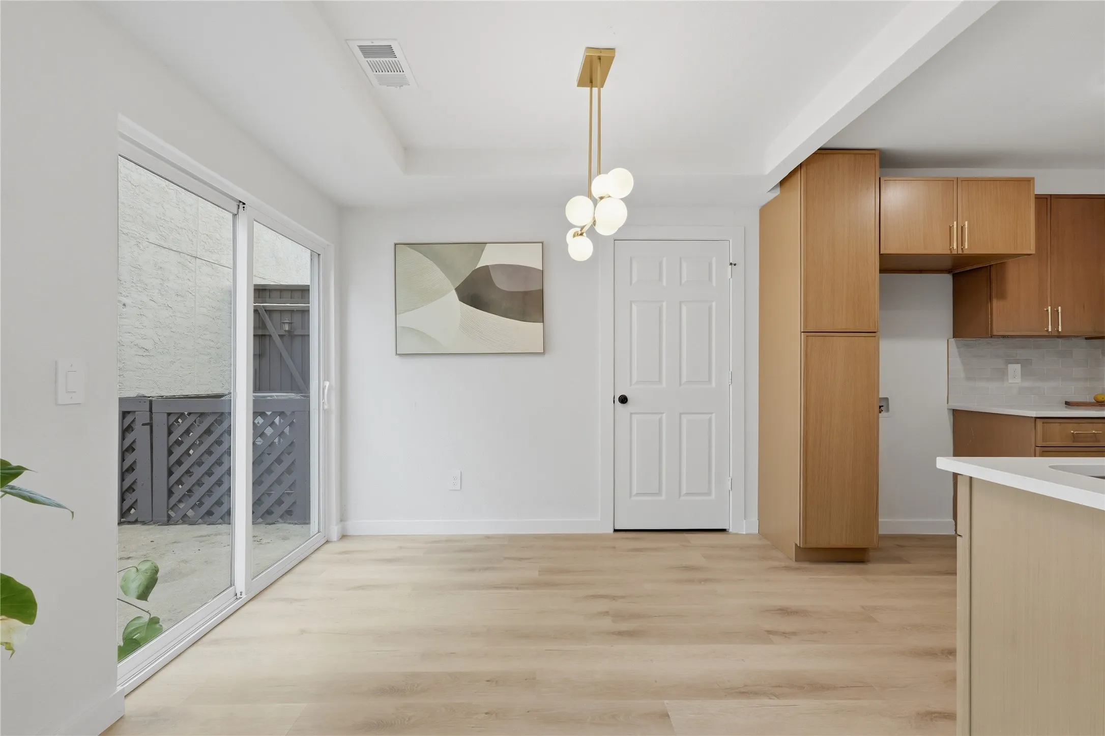 Open-concept living area featuring wood-finish flooring, a modern chandelier, and sliding glass doors leading to an outdoor patio