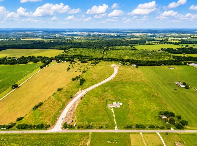 Expansive land parcel featuring a gravel access road, a single-story residence, and surrounding green fields