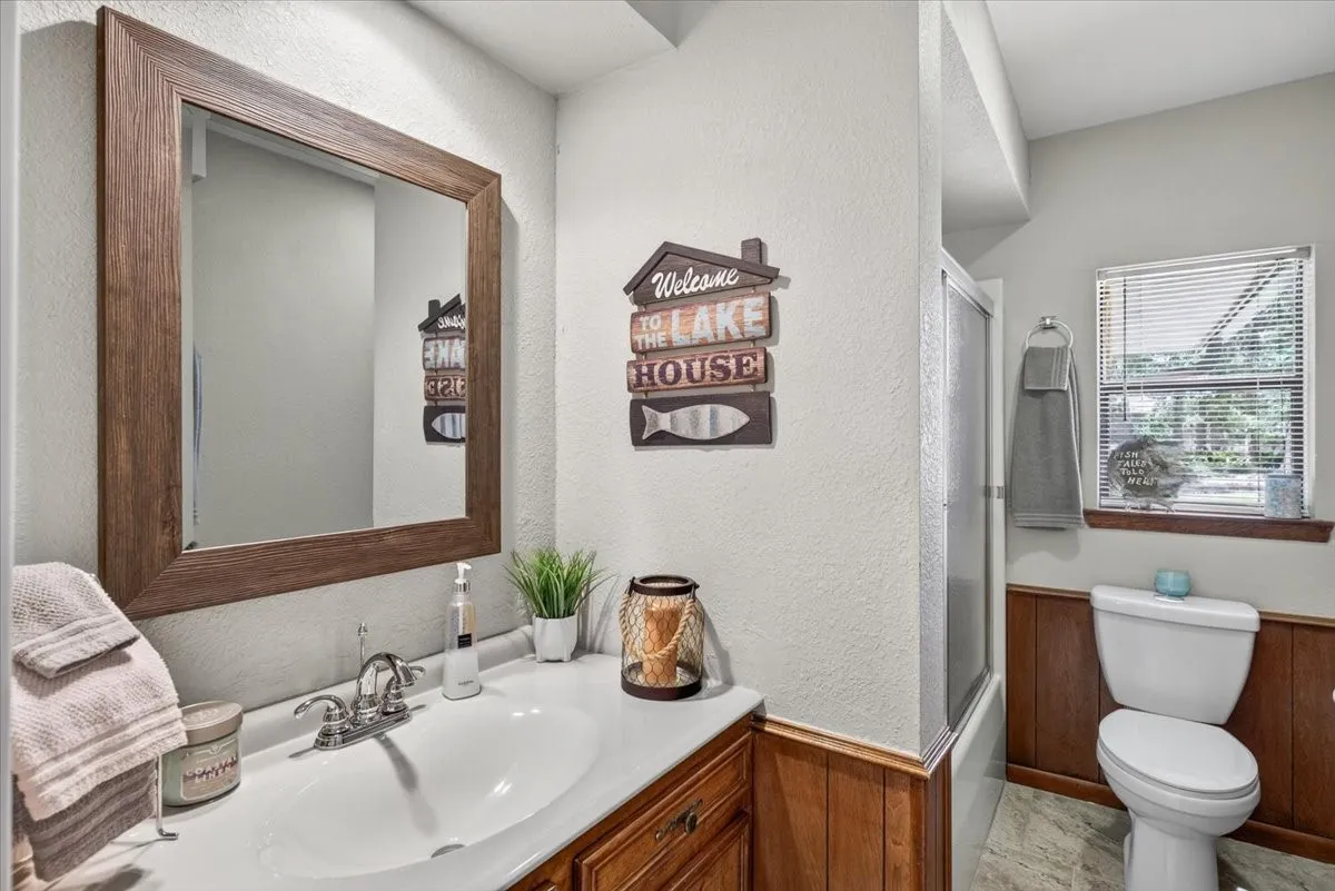 Bathroom featuring a wood-framed mirror, vanity with an integrated sink, chrome faucet, wood paneling, and a shower-tub combination with a sliding glass door