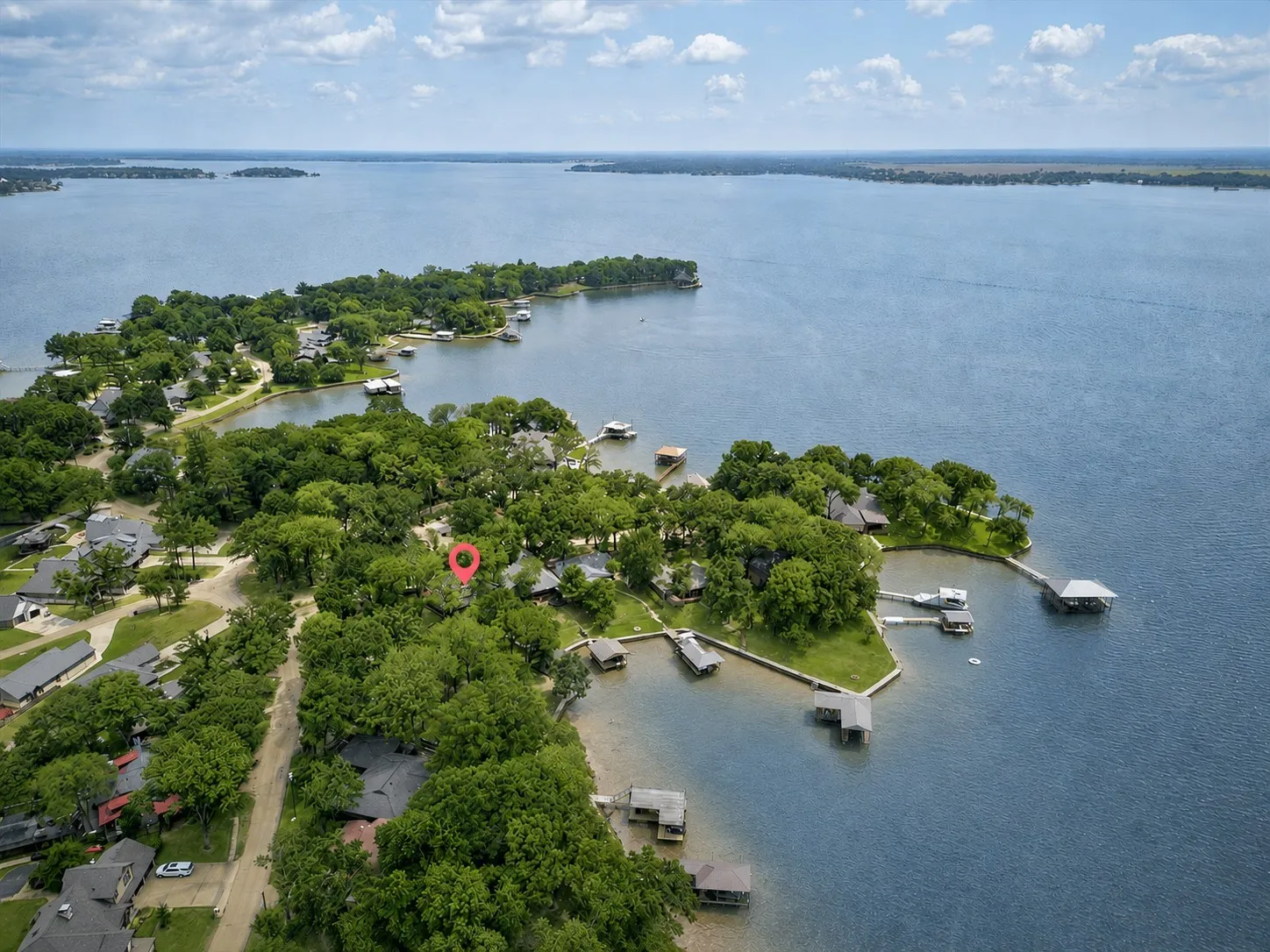 Aerial perspective of a lakeside property in a cove off of open water featuring extensive tree coverage, direct water access, and amazing sunset views.