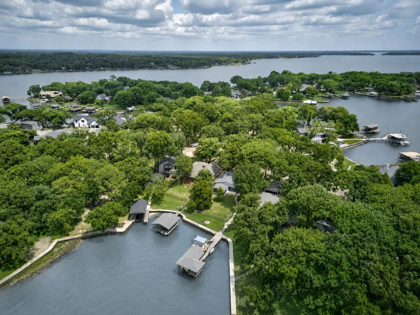 Aerial perspective of a lakeside property in a cove off of open water featuring extensive tree coverage, direct water access, and amazing sunset views.