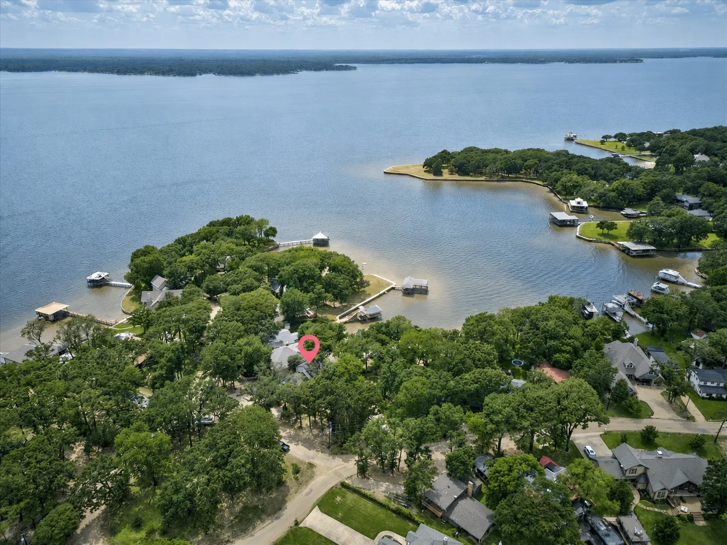Aerial perspective of a lakeside property in a cove off of open water featuring extensive tree coverage, direct water access, and amazing sunset views.