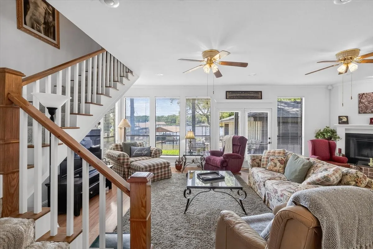 Spacious living area featuring large windows, double glass doors, a fireplace with a brick surround, and multiple ceiling fans, Upstairs is a second primary suite.