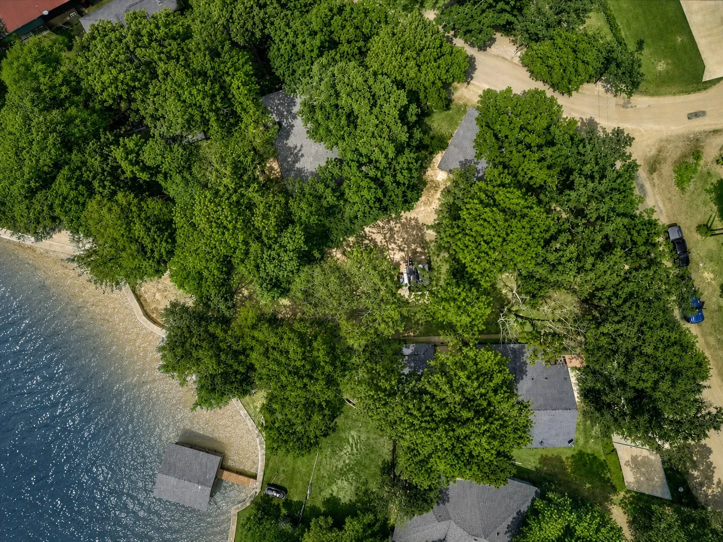 Aerial perspective of a lakeside property in a cove off of open water featuring extensive tree coverage, direct water access, and amazing sunset views.