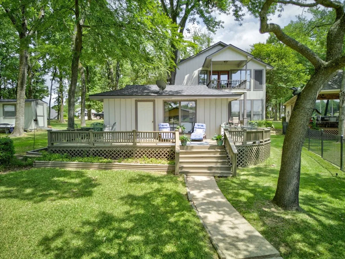 Lakeside view of the home feturing a pretty landscaped yard, mature shad trees, and expansive deck and balcony all on the lakeside.