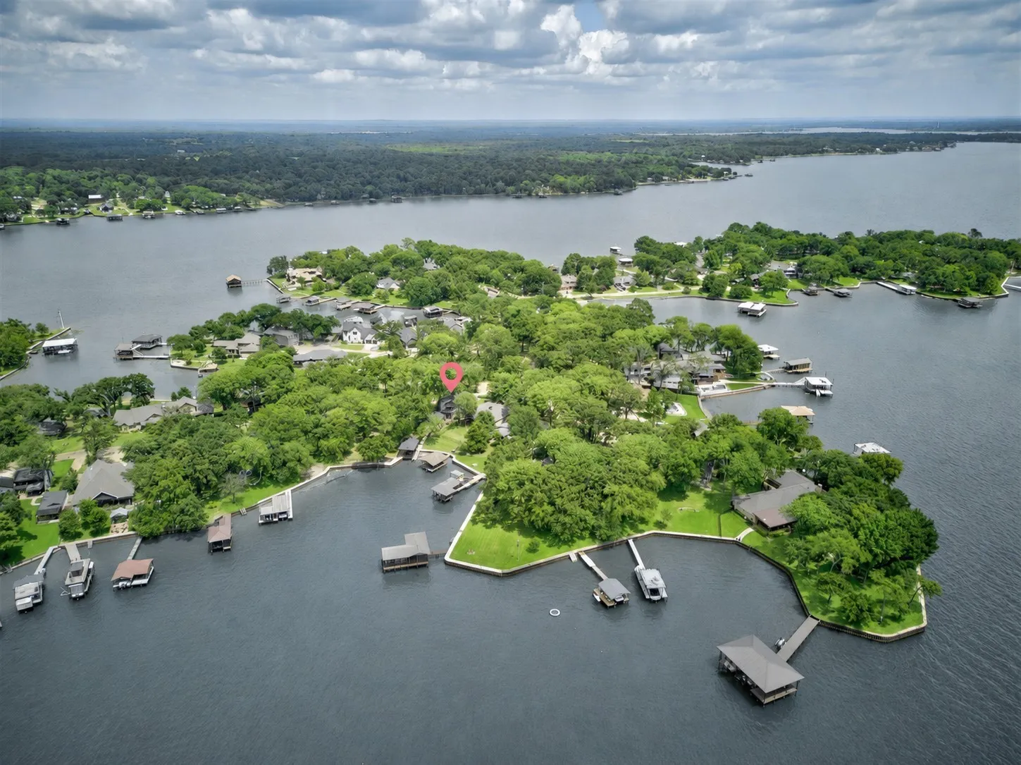 Aerial perspective of a lakeside property in a cove off of open water featuring extensive tree coverage, direct water access, and amazing sunset views.