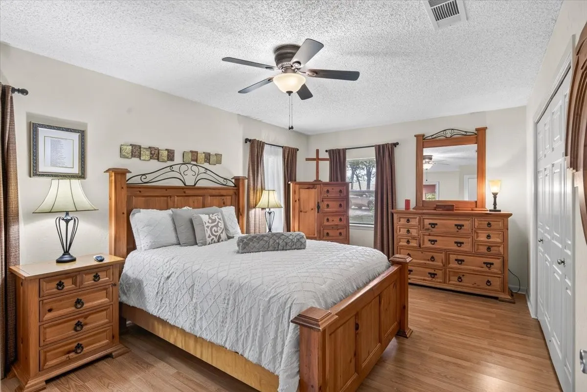 First floor Primary Bedroom featuring oak flooring, neutral colors, ceiling fan with integrated lighting, and multiple windows with blinds and ensuite bath.