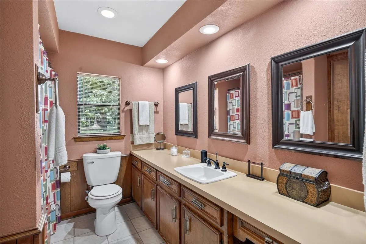 First floor ensuite bath in the first primary bedroom featuring a dual-sink vanity with wood cabinetry, framed mirror and tub-shower