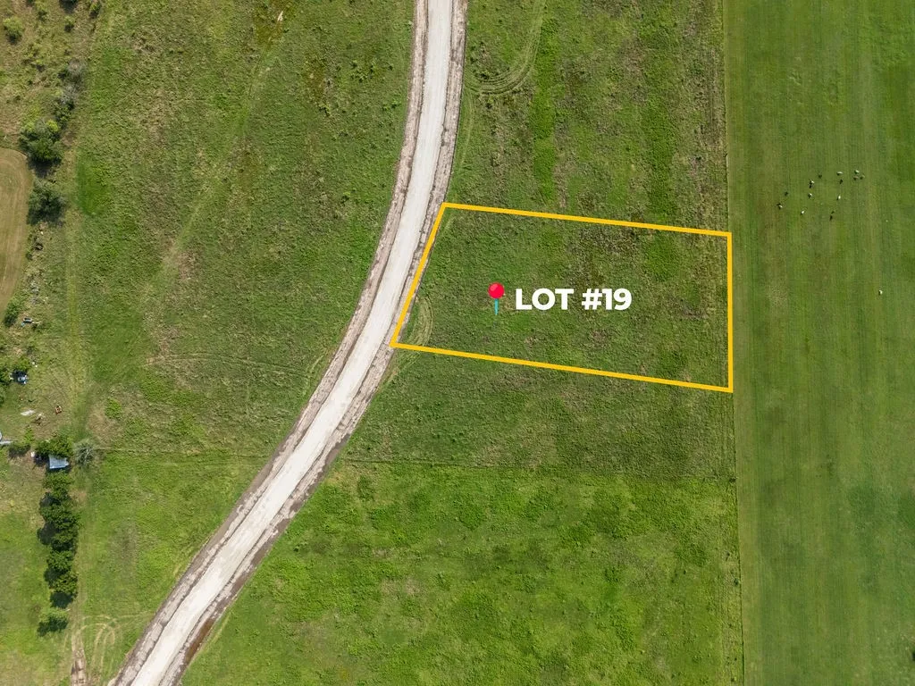 Cleared land parcel with a designated boundary, featuring a gravel road frontage and surrounding expansive green fields