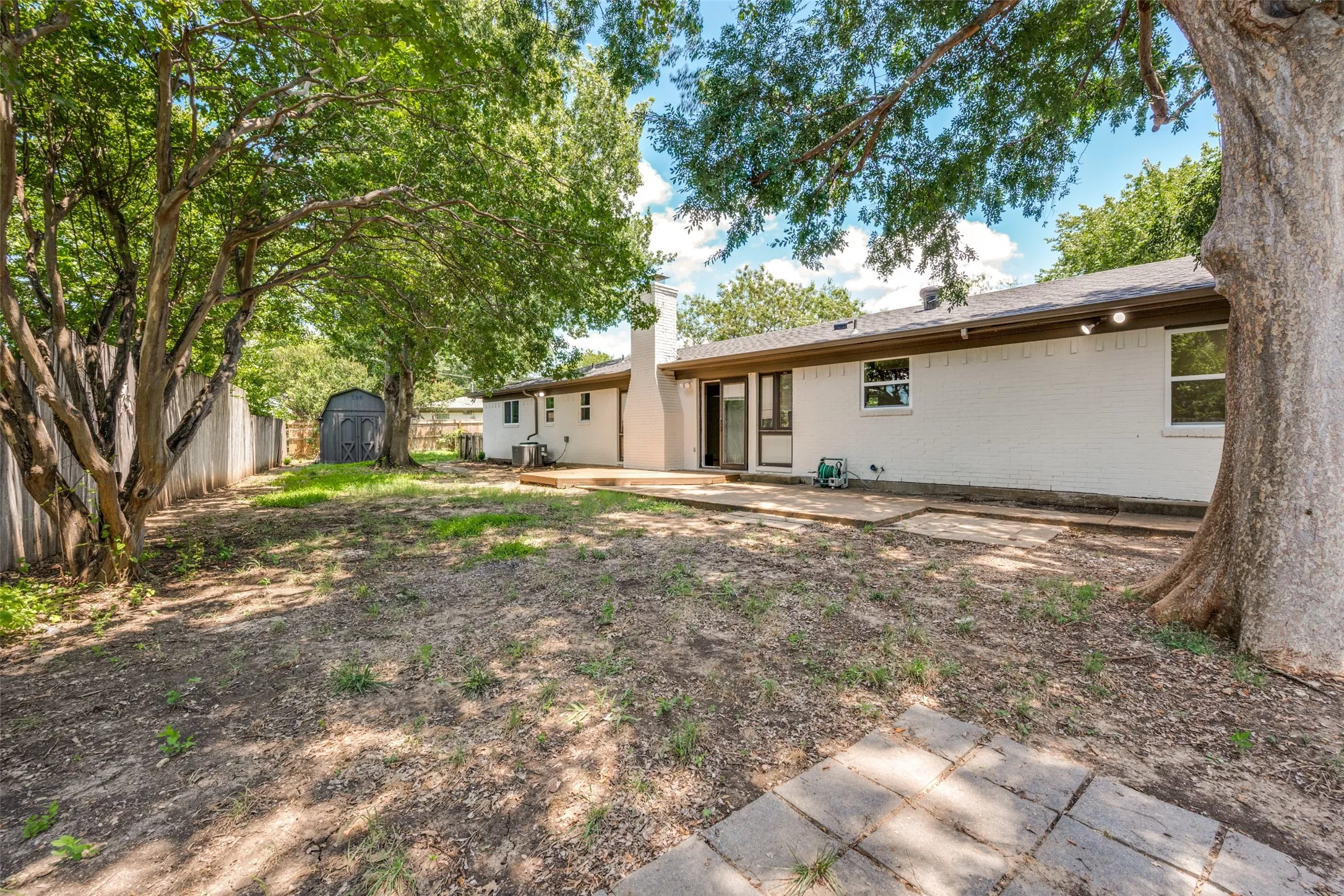 Expansive backyard featuring mature trees, a wooden privacy fence, a detached shed, a wooden deck, and a concrete patio