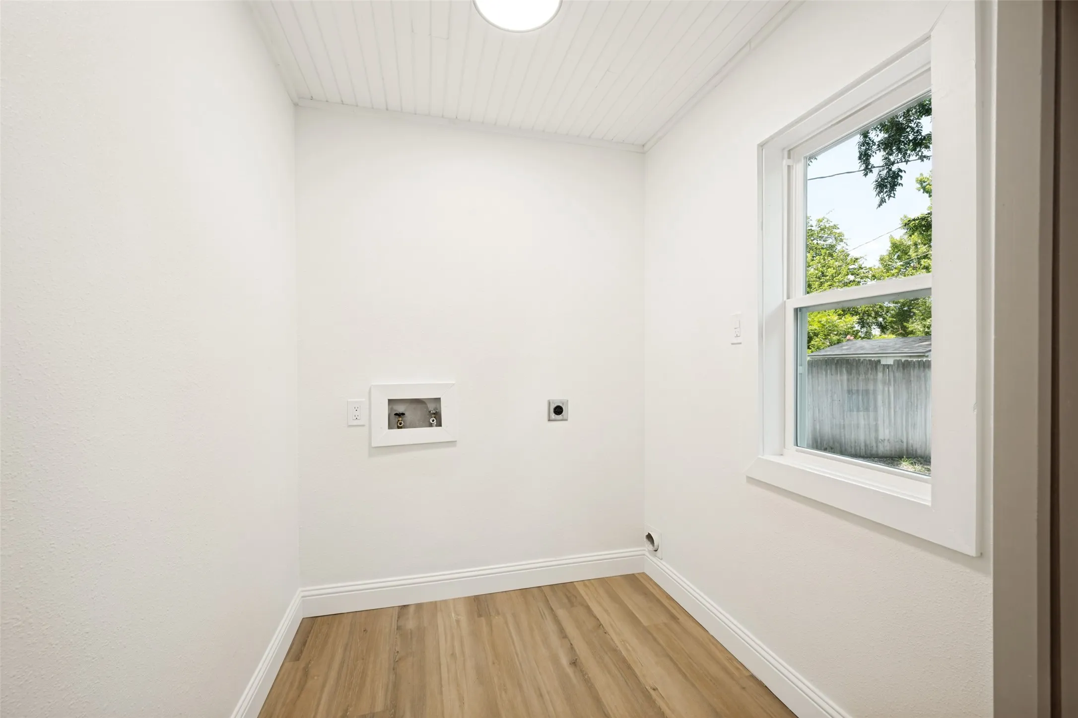 Laundry room featuring wood-finish flooring, a double-hung window, and a beadboard ceiling