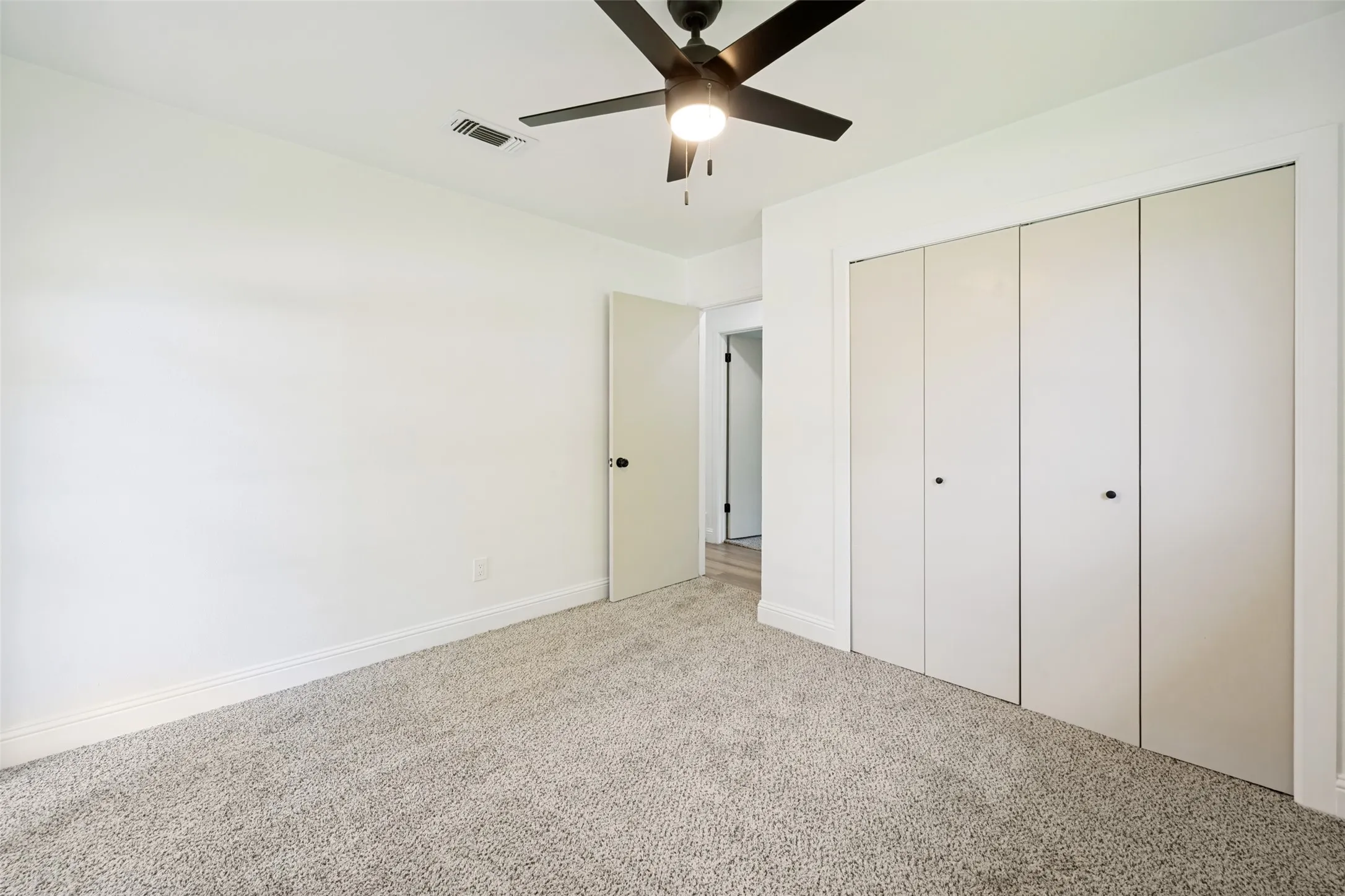 Carpeted room featuring a ceiling fan with integrated lighting, a spacious bi-fold door closet, white walls, and white trim