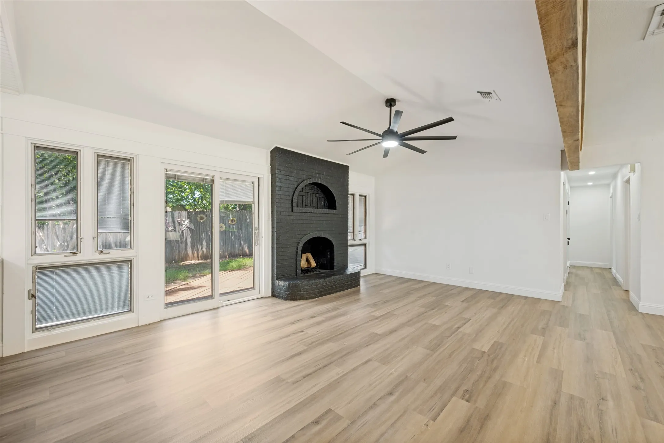 Spacious room featuring wood-finish flooring, a modern ceiling fan, and a black brick fireplace