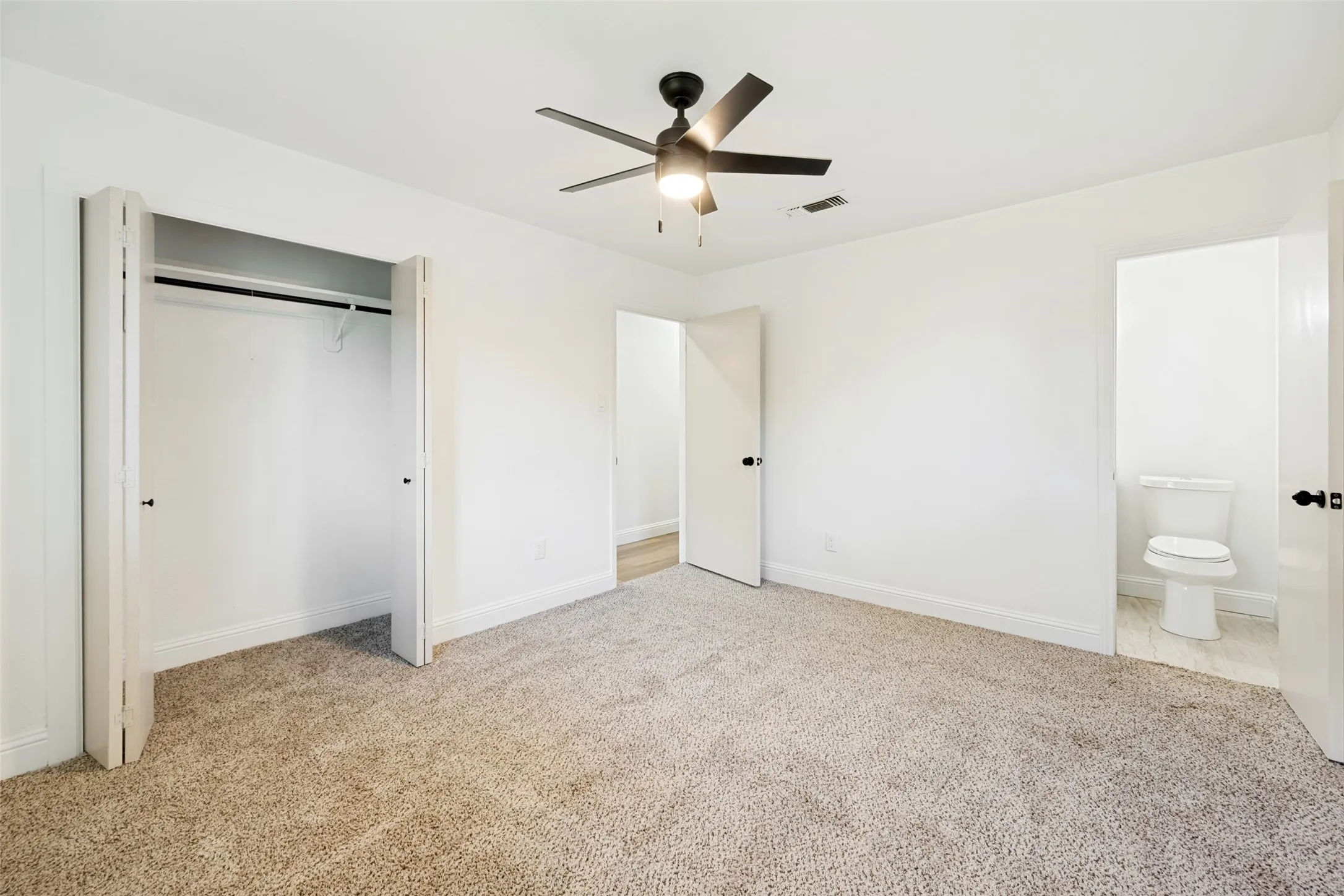 Bright interior room featuring a neutral carpet, white walls, and a contemporary ceiling fan with integrated lighting